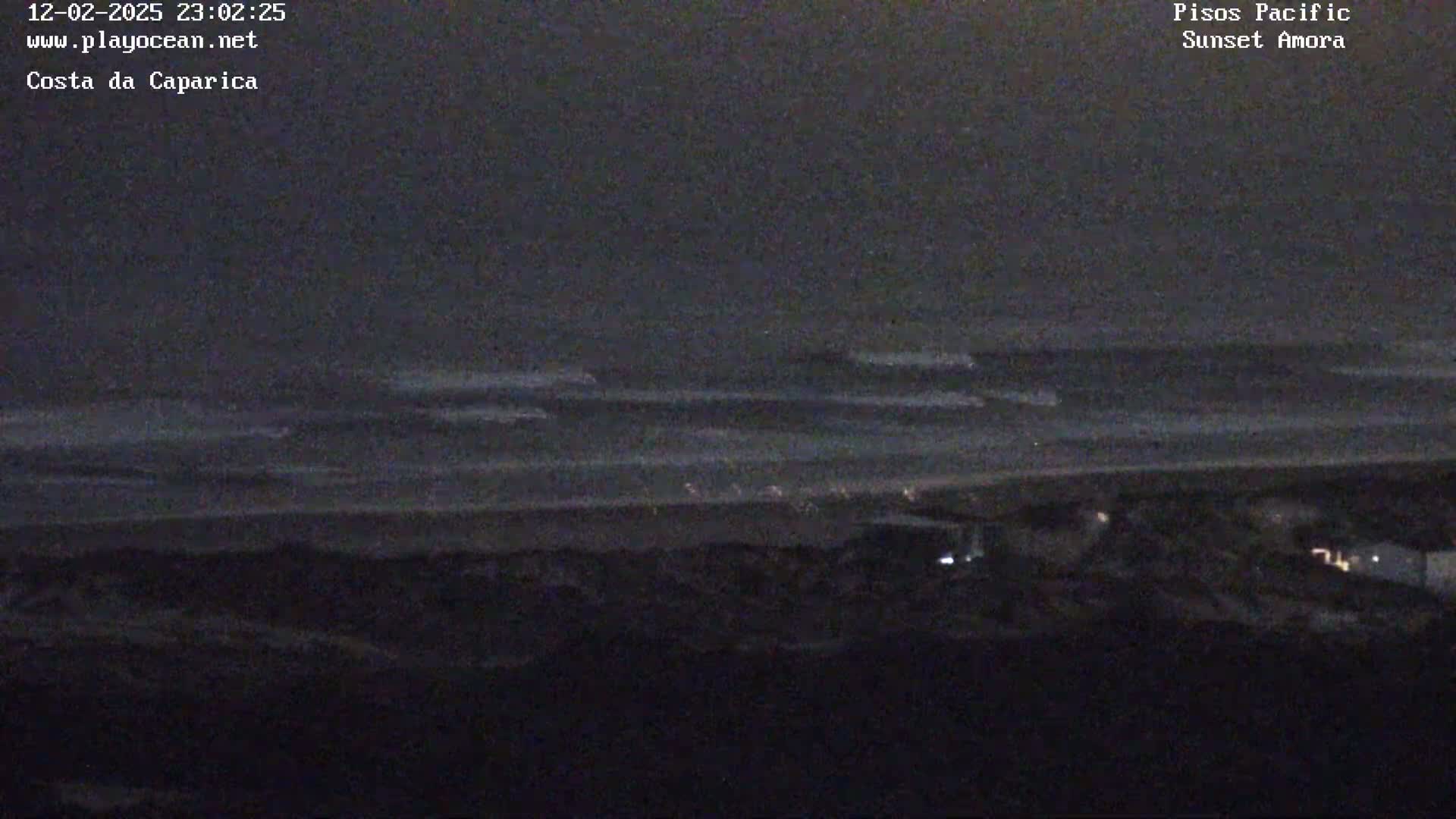 A dark, nighttime view shows a beach with small waves lapping the shore under a cloudy sky.