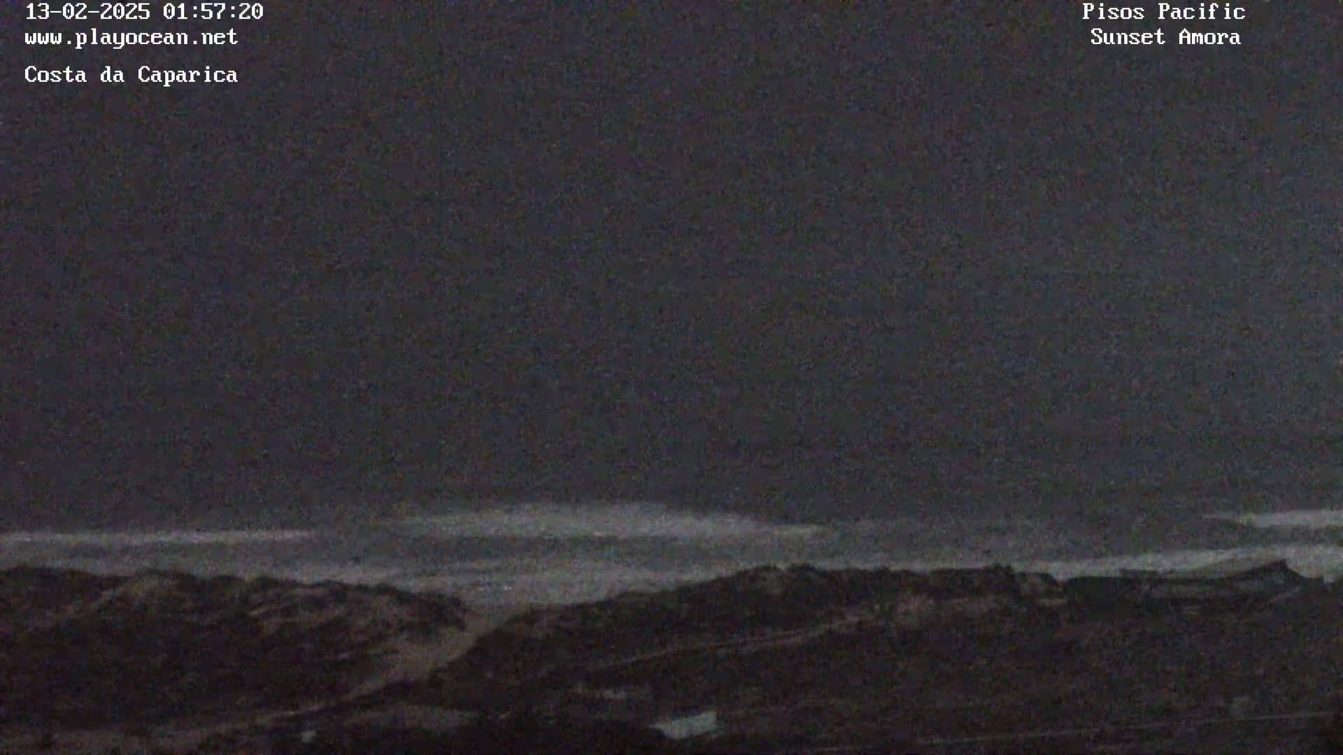 A dark, nighttime view of a coastline shows a relatively calm ocean under a mostly clear, dark sky.