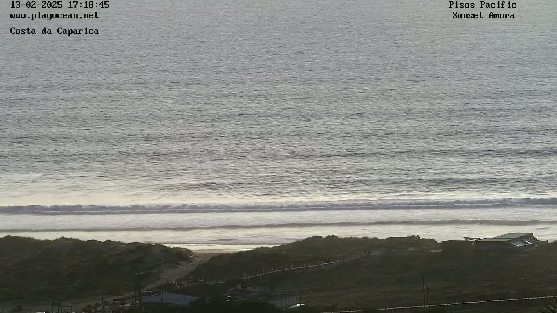 A long line of waves rolls onto a sandy beach under a cloudy sky.