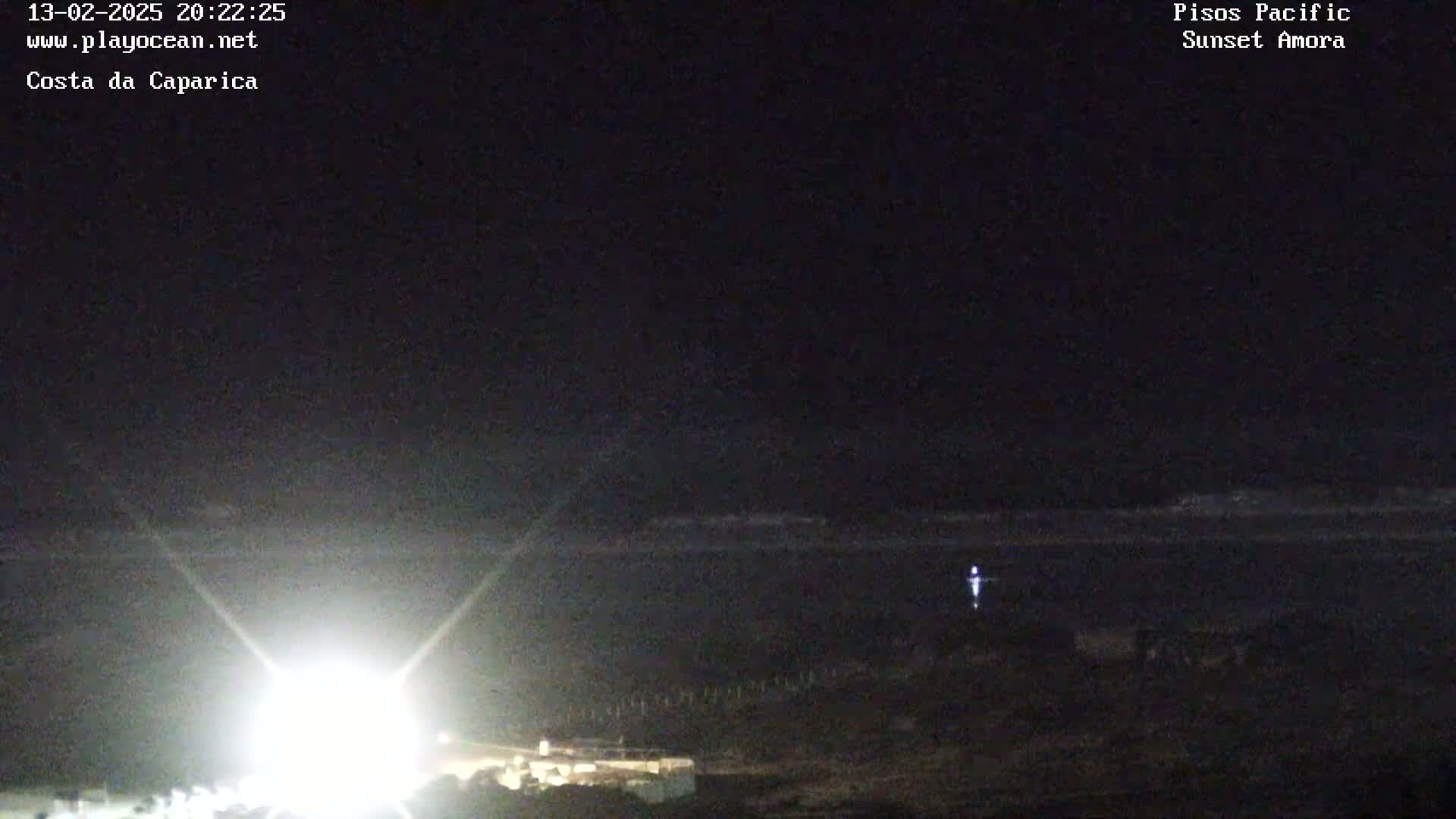 A nighttime coastal scene shows a bright light source in the foreground, a dark ocean with a faint light on the horizon, and dark land in the bottom right corner.