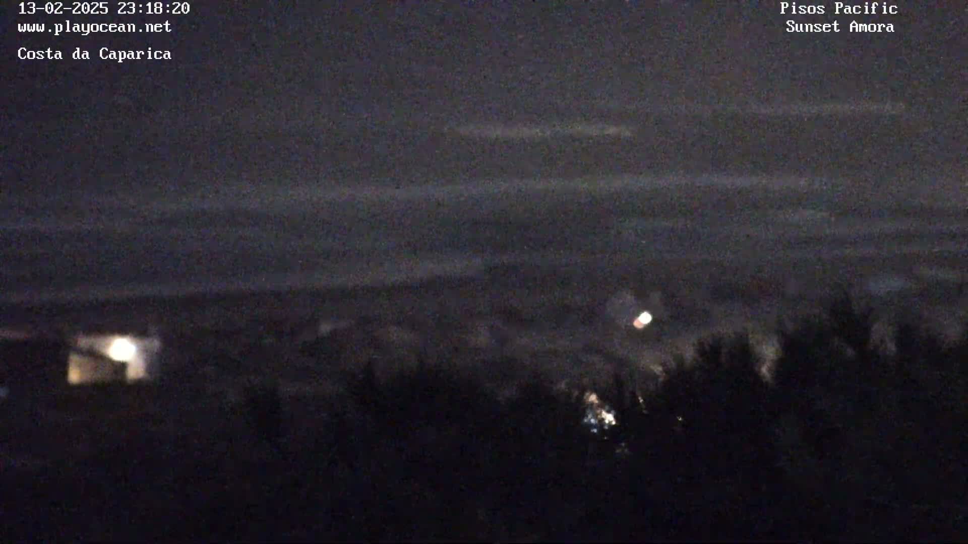 A nighttime, low-light view of a dark ocean under a mostly clear sky with a few faint lights visible on land.