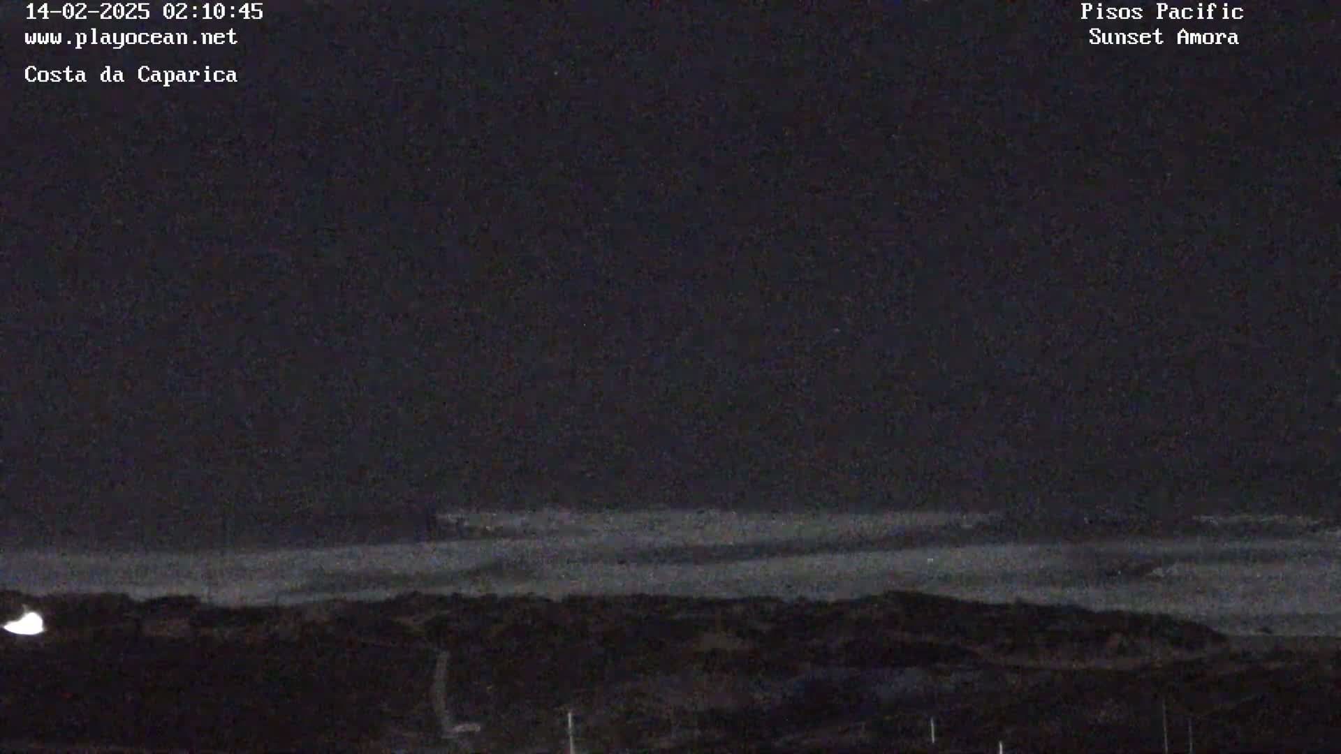 A dark, nighttime view of a shoreline with a calm ocean under a mostly clear sky.