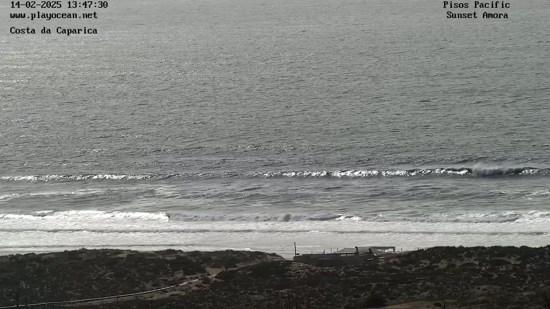 A high-angle view shows a beach with moderate waves rolling onto the shore on an overcast day.