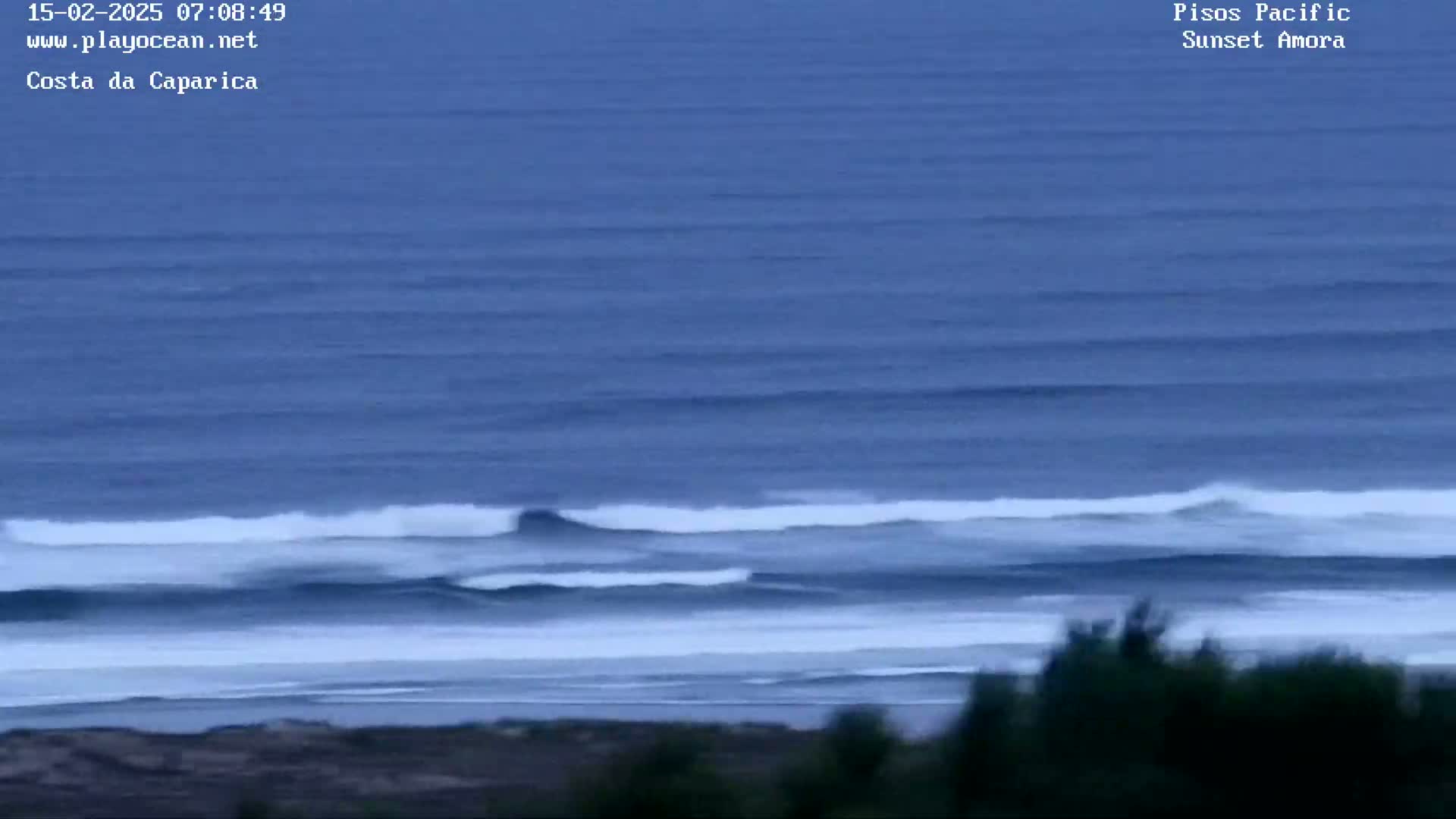 A long view of ocean waves breaking on a beach under an overcast sky.