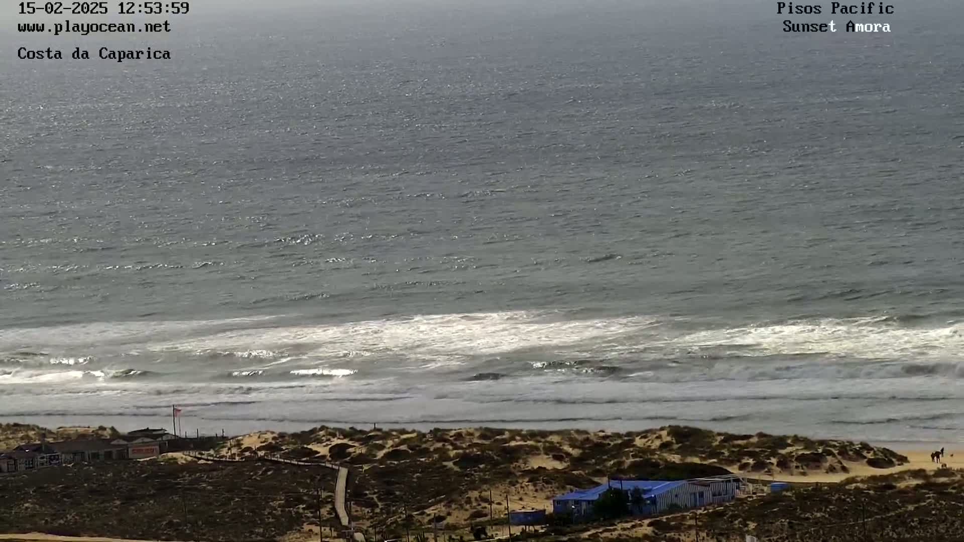 A wide shot of a sandy beach with waves breaking on the shore, under a mostly cloudy sky.