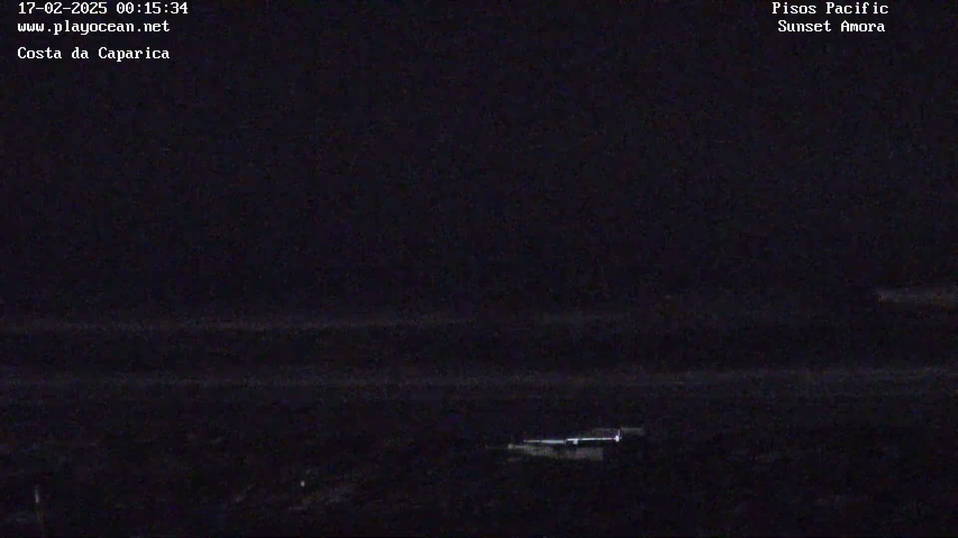 A dark, nighttime view of a beach with a faintly visible shoreline and a small structure in the lower right corner.