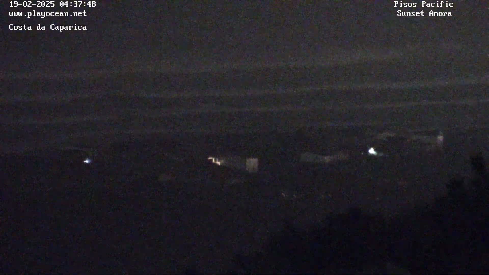 A dark nighttime view shows a distant, dark ocean under a mostly clear sky with a few faint lights visible on the shore.