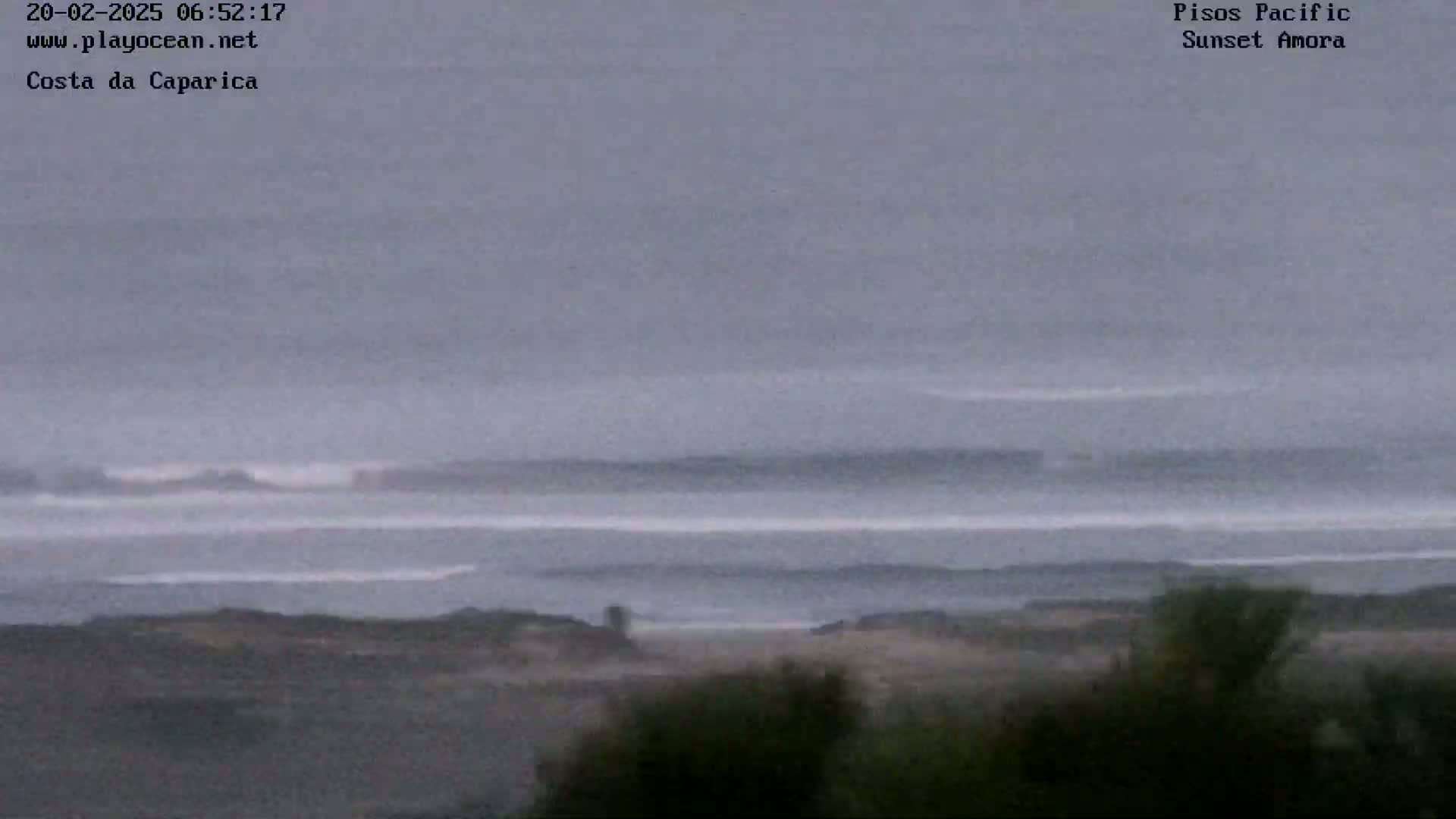 A long shot shows an overcast sky over a grey ocean with small waves breaking near a dark shoreline.