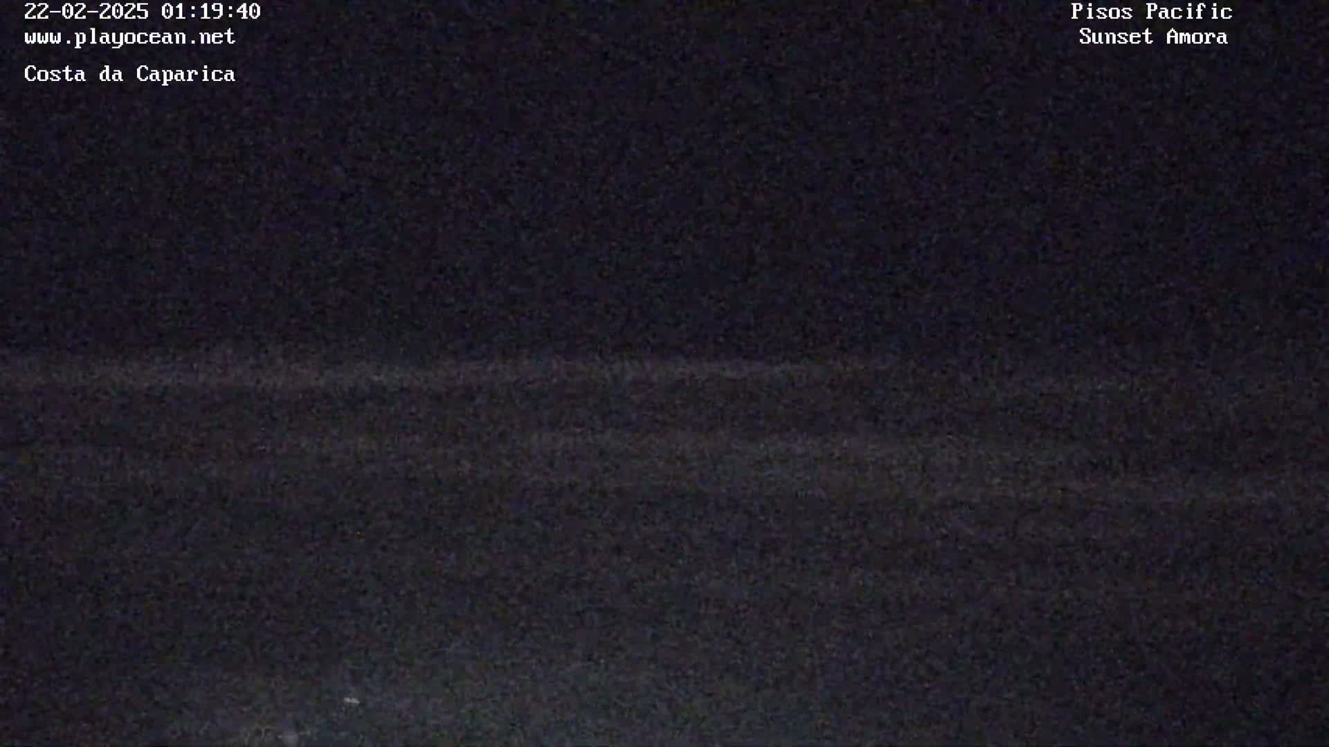 A dark, nighttime view of a coastline with a faint horizon line.