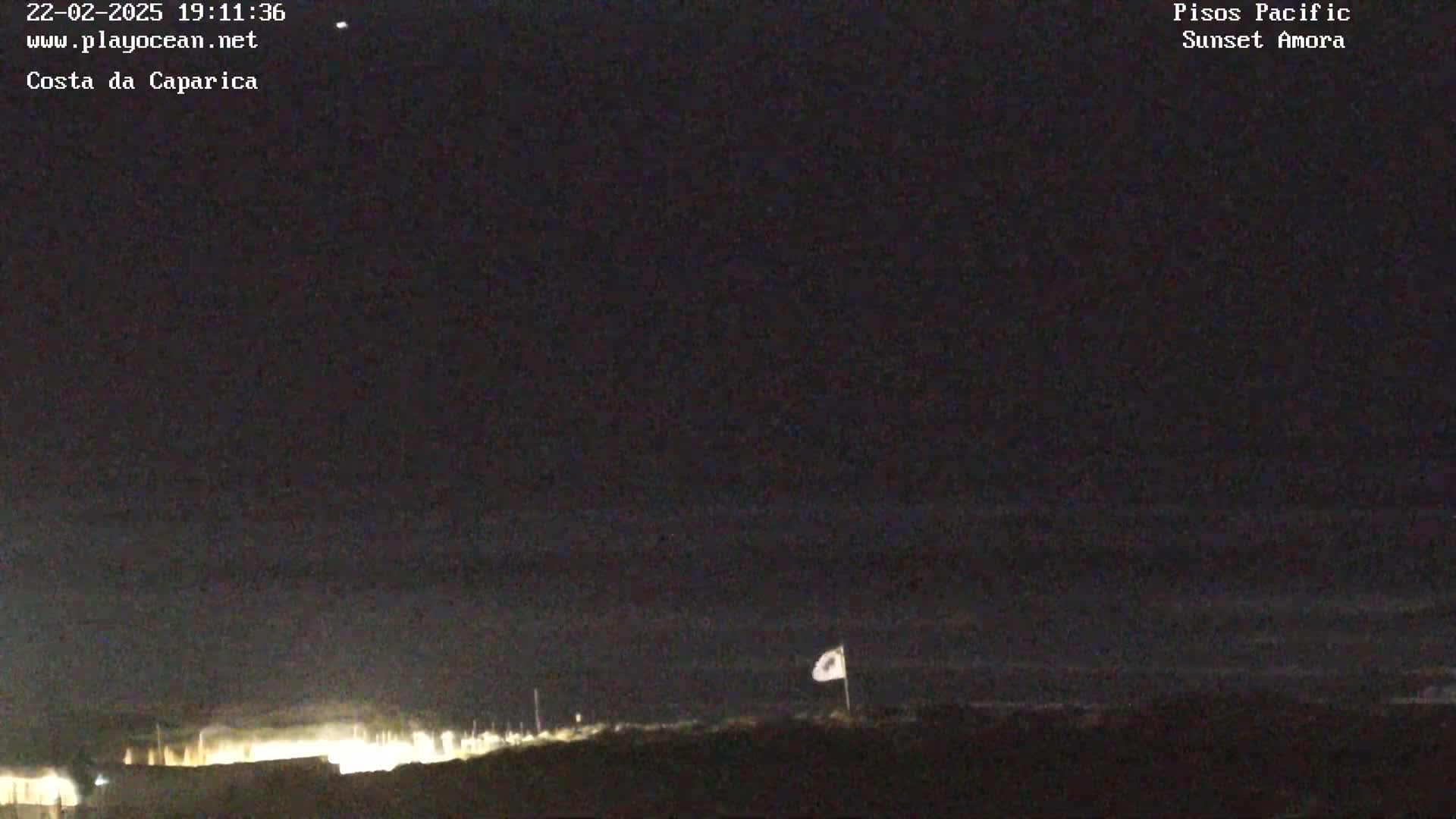 A nighttime, low-light view of a coastline with a flagpole and a faintly visible body of water under a dark sky.