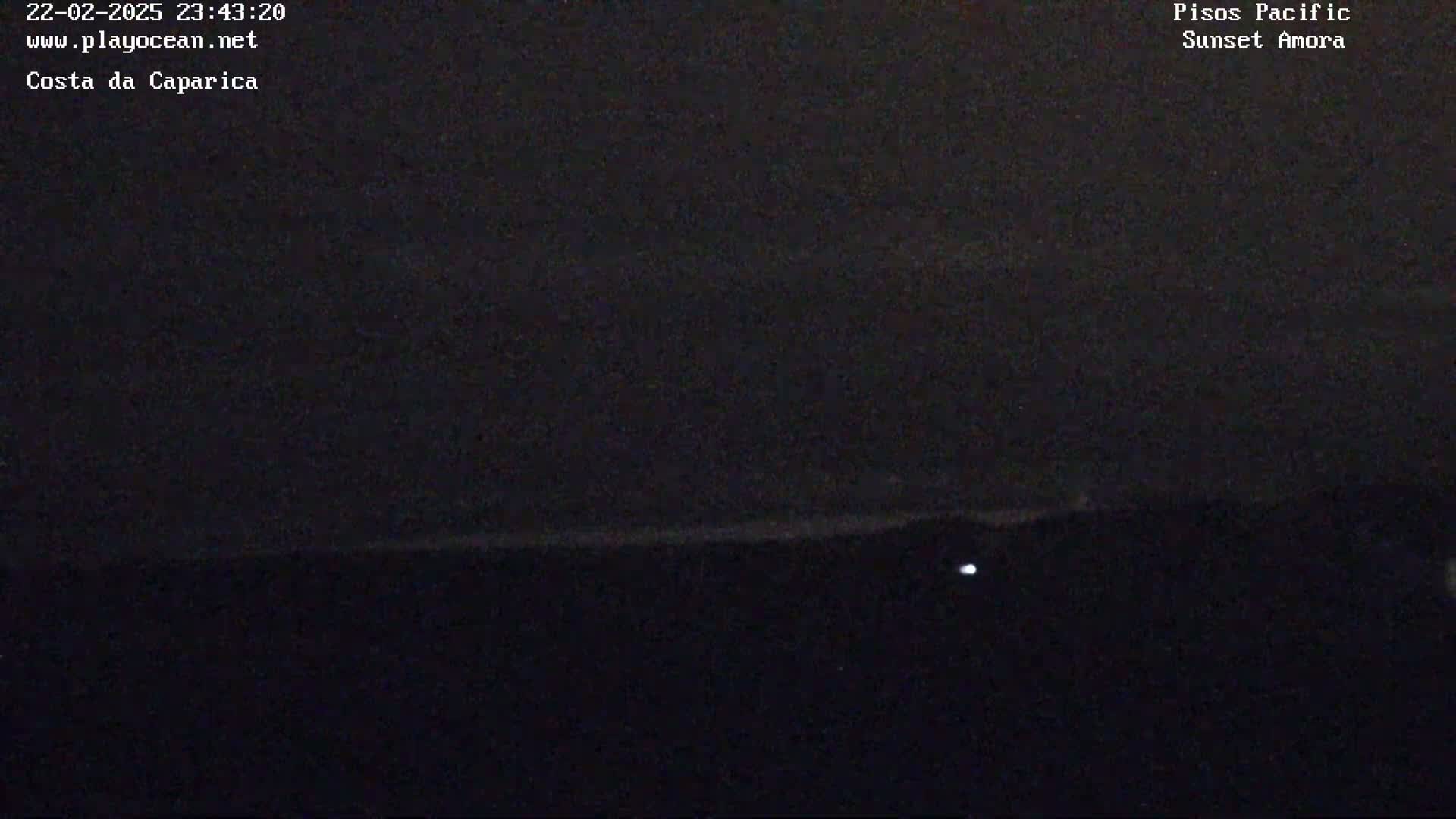 A dark nighttime coastal scene shows a faint horizon line with a single small light visible in the lower portion of the frame.
