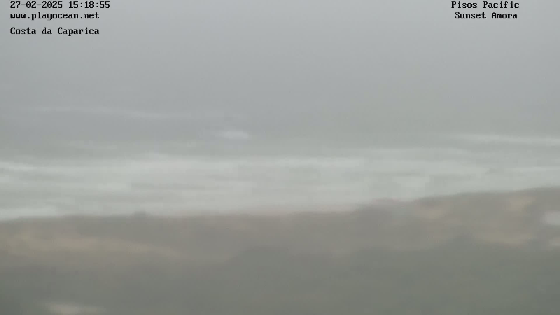 A hazy, overcast day shows a beach with waves gently rolling into the shore.