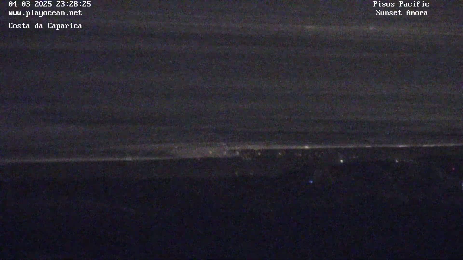 A nighttime, long shot of a dark ocean with a faint line of lights visible on the horizon.