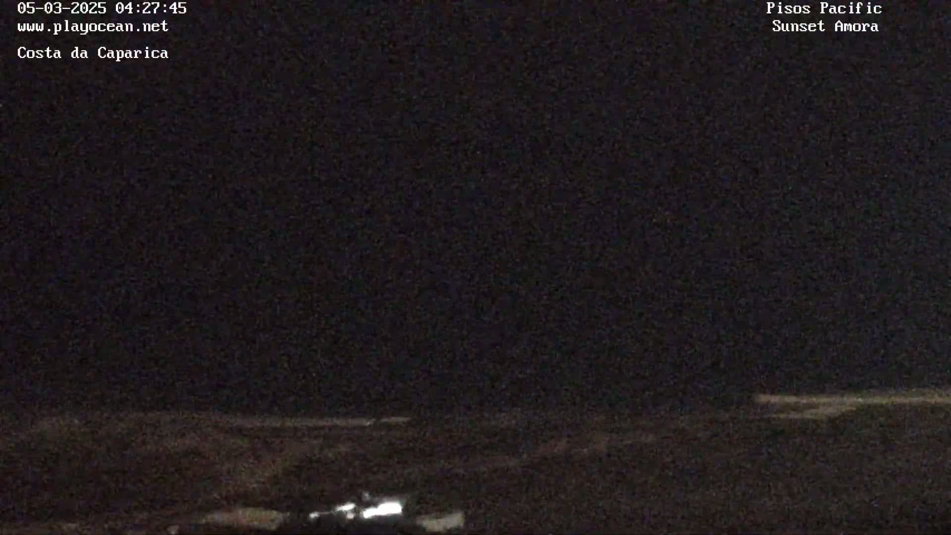 A nighttime, dark outdoor scene shows a mostly flat, dark landscape with a few faint lights visible in the distance.