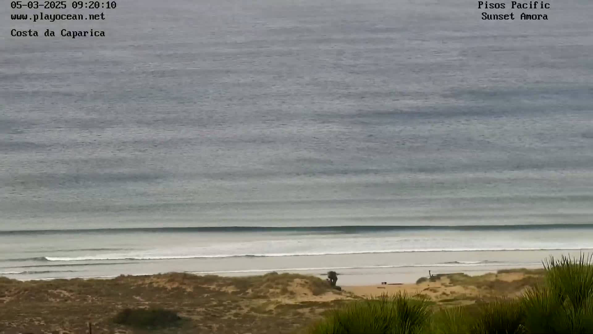 An overcast sky overlooks a sandy beach with small waves rolling into shore.