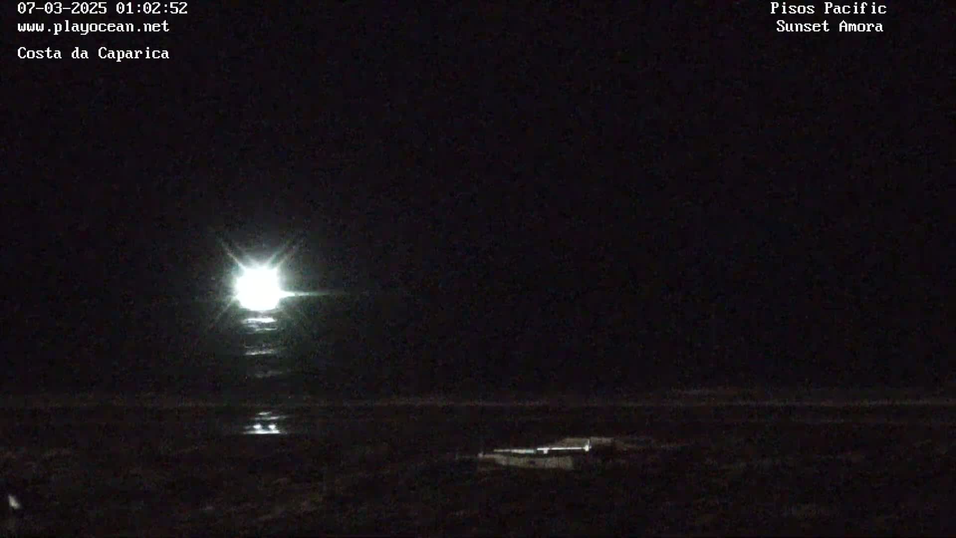 A bright light, possibly a ship's light, shines on the dark ocean at night.