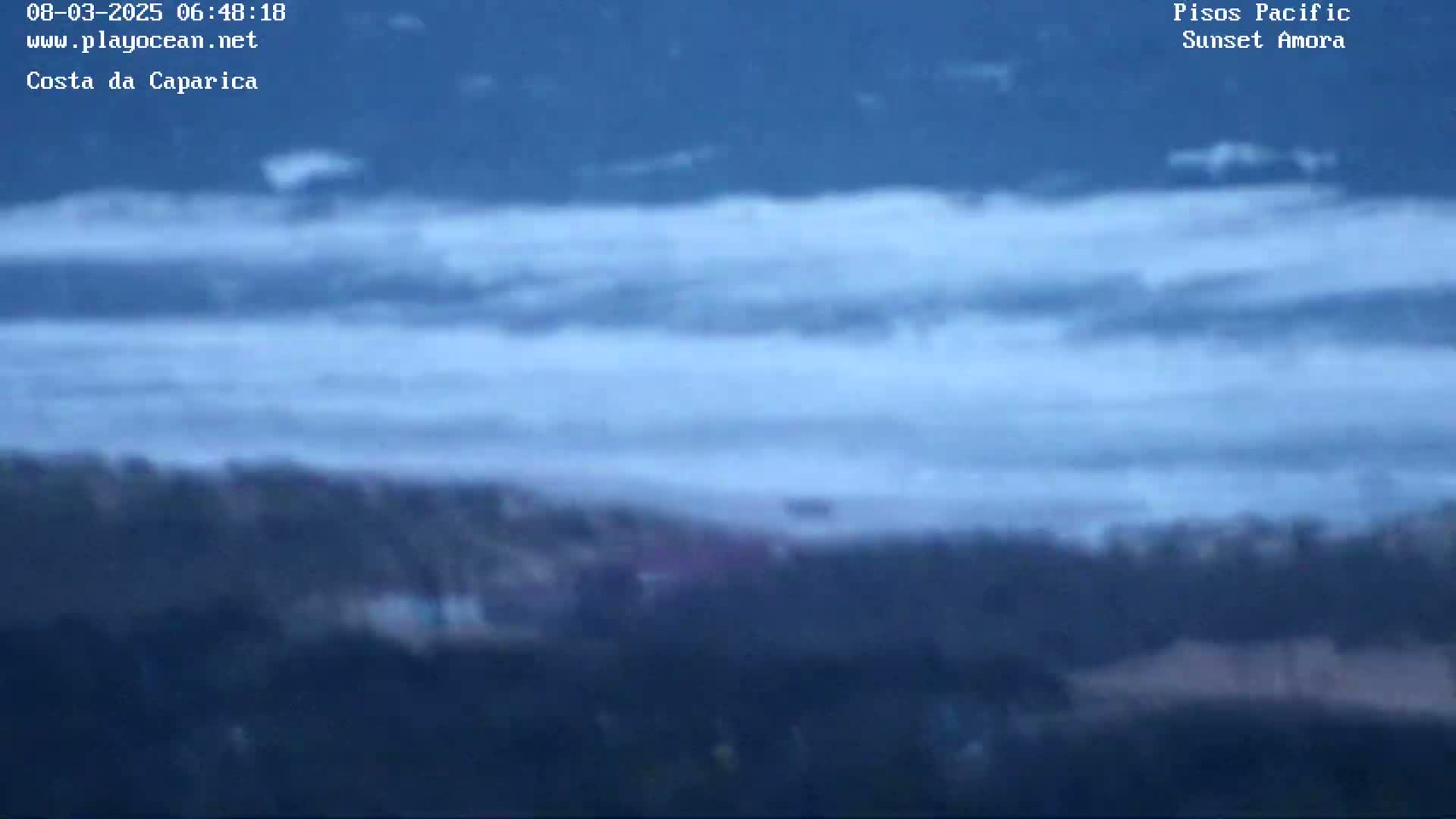 A blurry long shot shows a stormy ocean with choppy waves crashing on a shoreline with dark sand or vegetation.