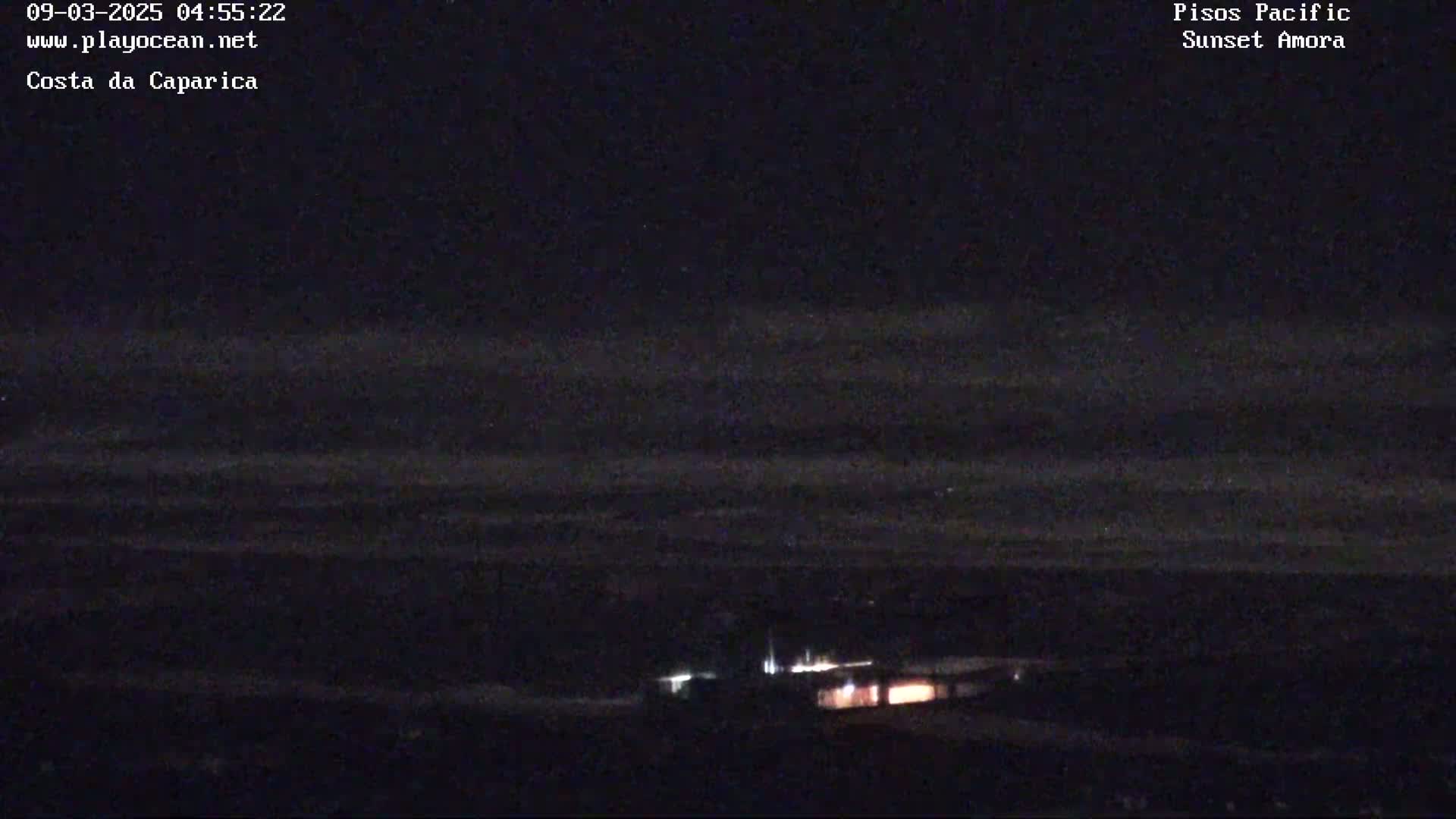 A nighttime long shot shows dimly lit buildings near a dark, possibly wavy, horizon under a dark sky.