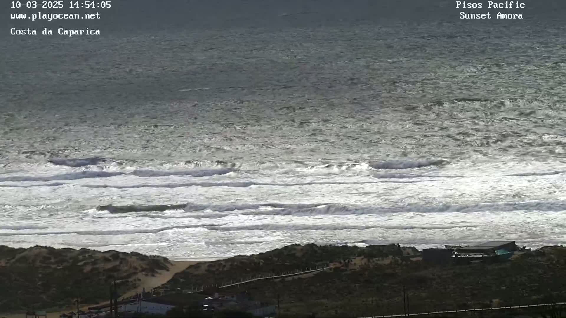 A view of a sandy coastline with moderate waves rolling into shore on an overcast day.