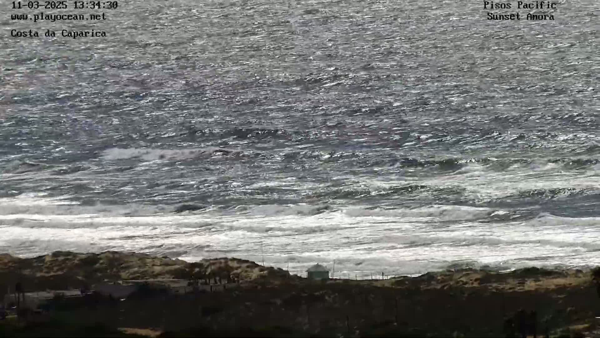 A view of a rocky shoreline with choppy waves crashing on the beach under a somewhat overcast sky.