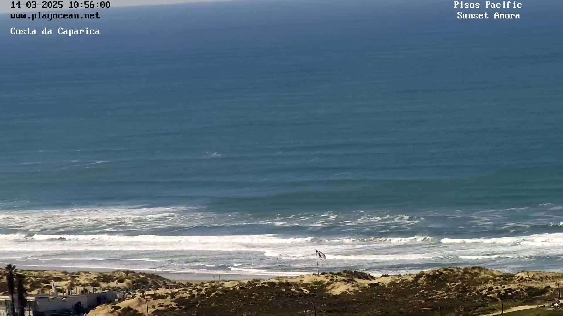 A high-angle view shows a sandy beach with rolling waves under a clear sky.