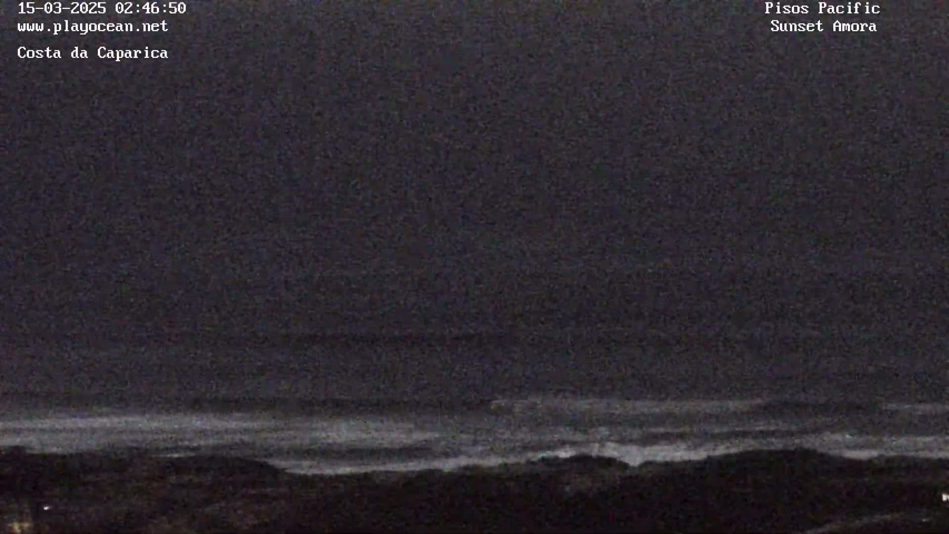 A dark, nighttime view of a wavy ocean under a cloudy sky.