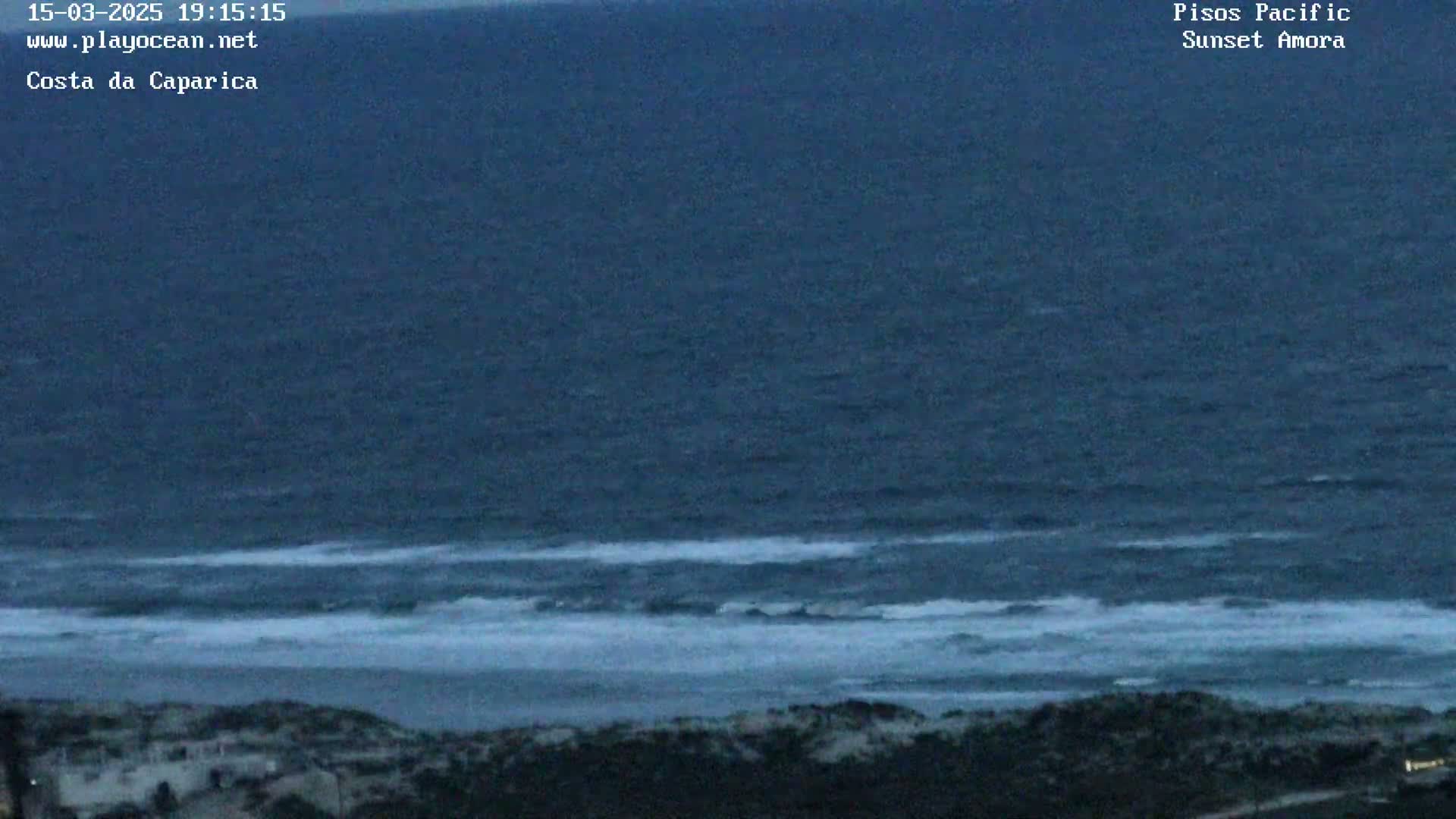 A dark, somewhat overcast view of a wavy ocean meeting a dark shoreline at dusk.