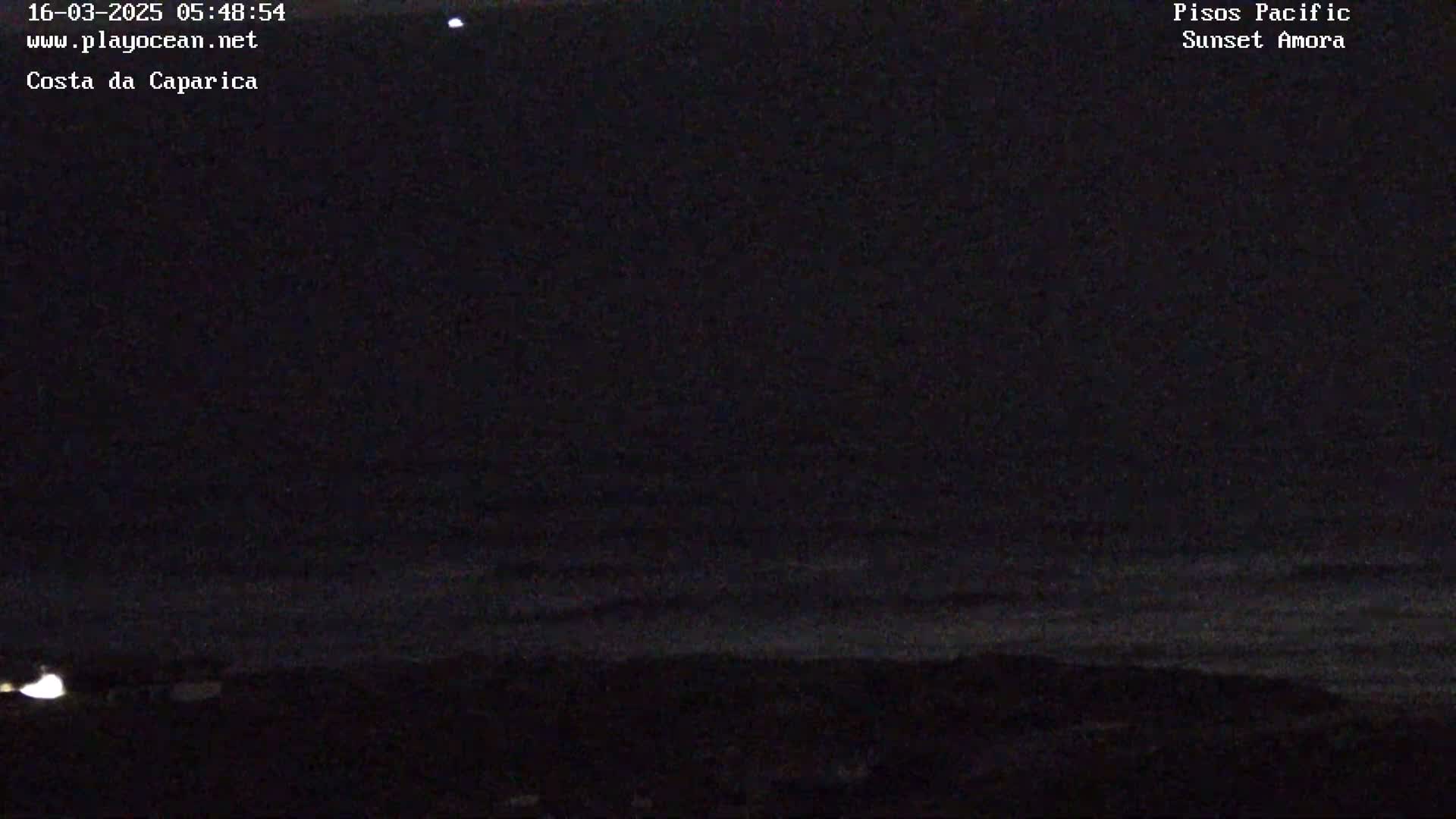 A dark nighttime scene shows a dark ocean meeting a dark shoreline under a mostly clear sky.