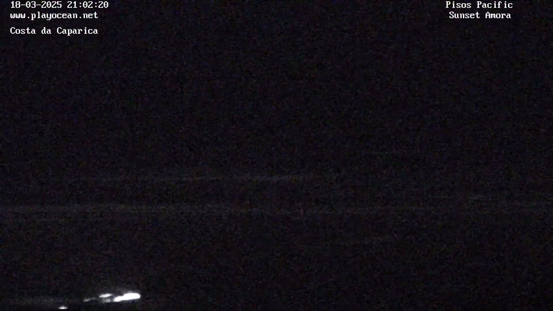 A nighttime, low-light image shows a dark ocean horizon with a faint, bright line possibly indicating lights on the water.