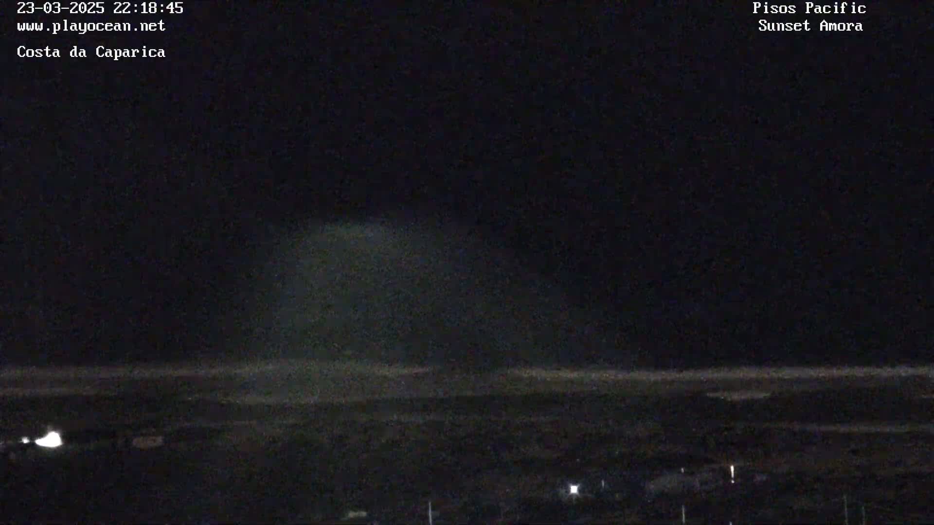 A nighttime, long shot of a beach with a faint, diffuse light source above the horizon.