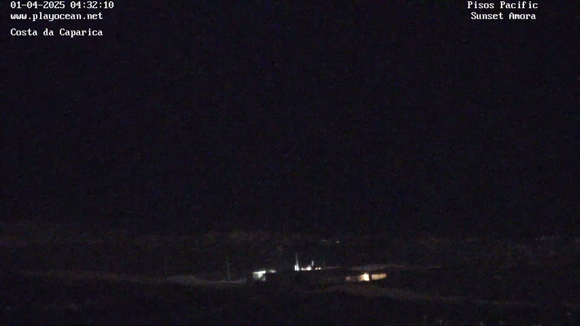A nighttime, dark outdoor scene shows a few distant lights on a low hill.