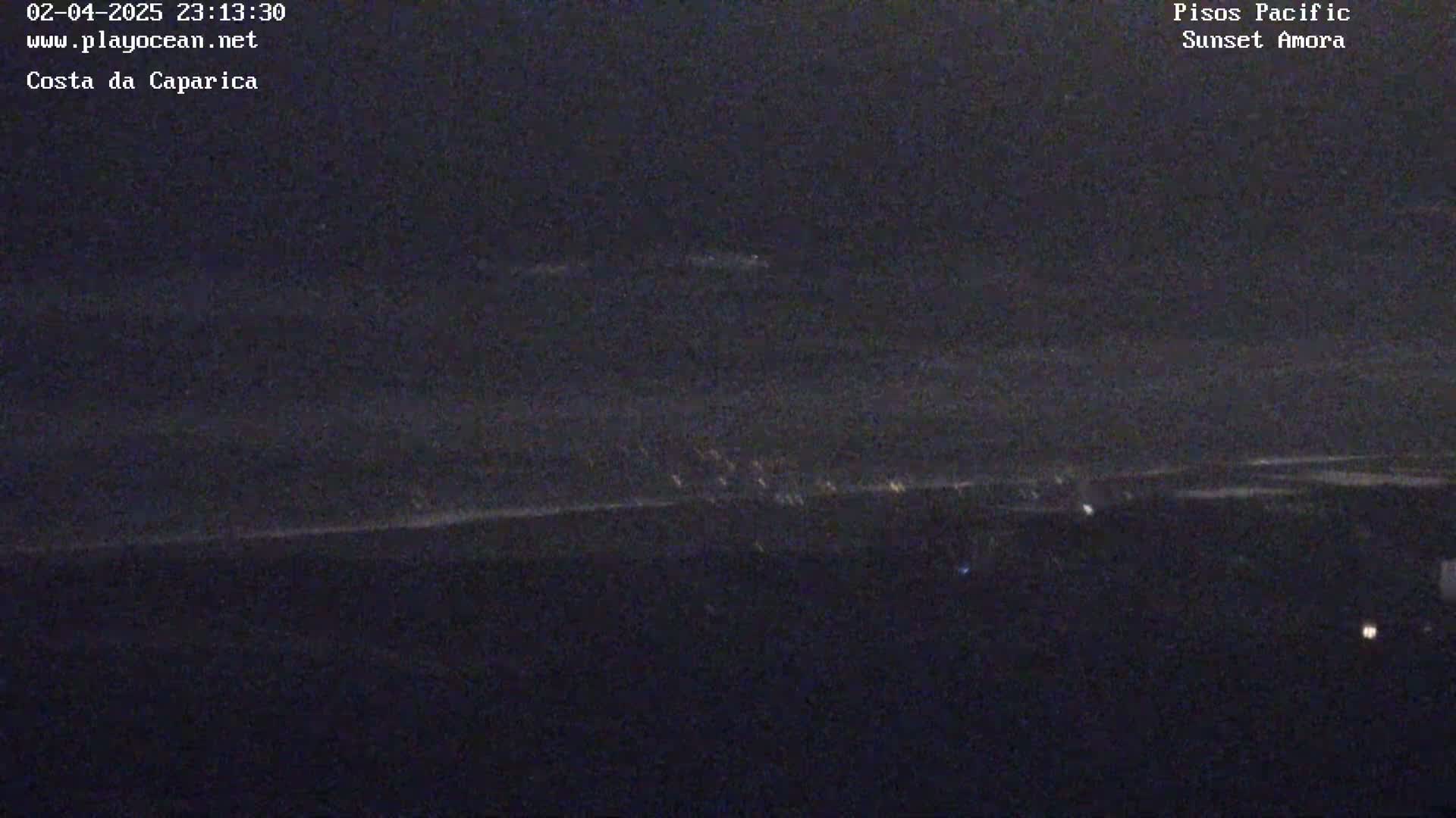A dark nighttime coastal scene shows a faint line of lights along the horizon over a dark body of water.