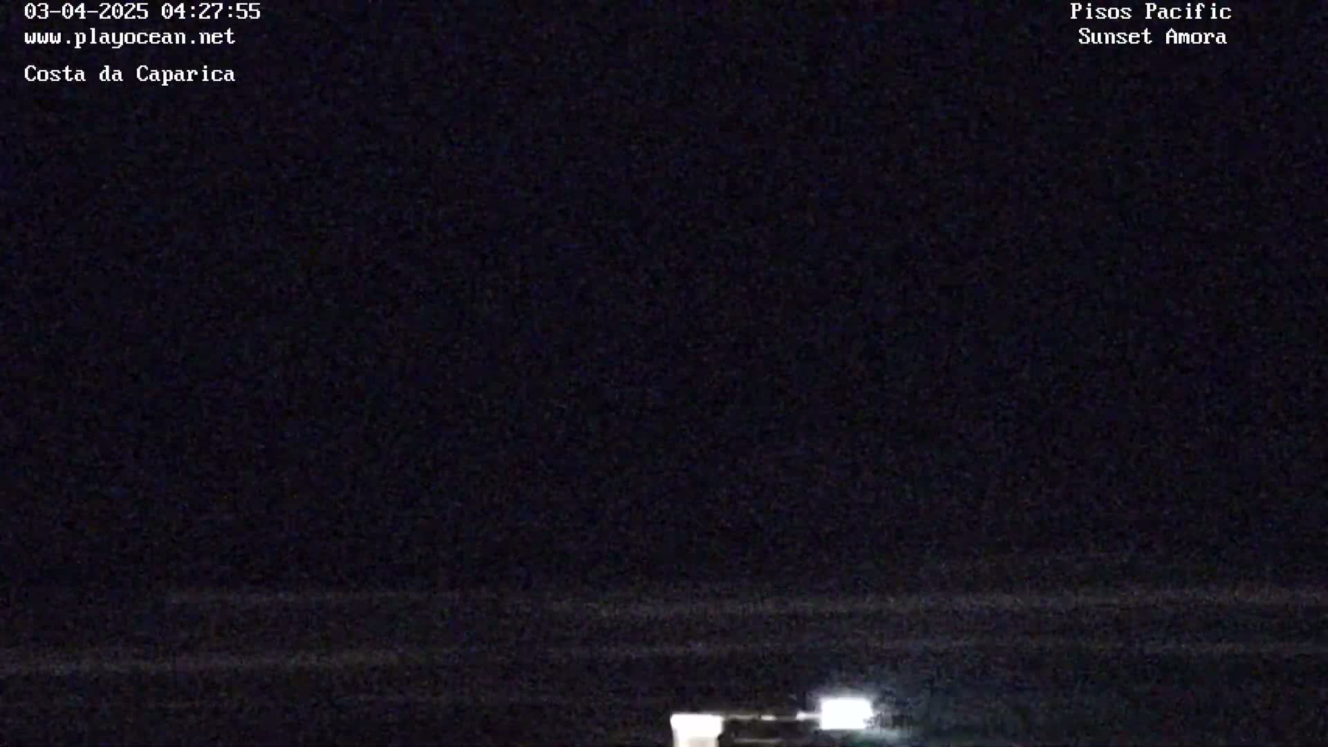 A dark nighttime scene shows a body of water with faintly lit structures in the distance.
