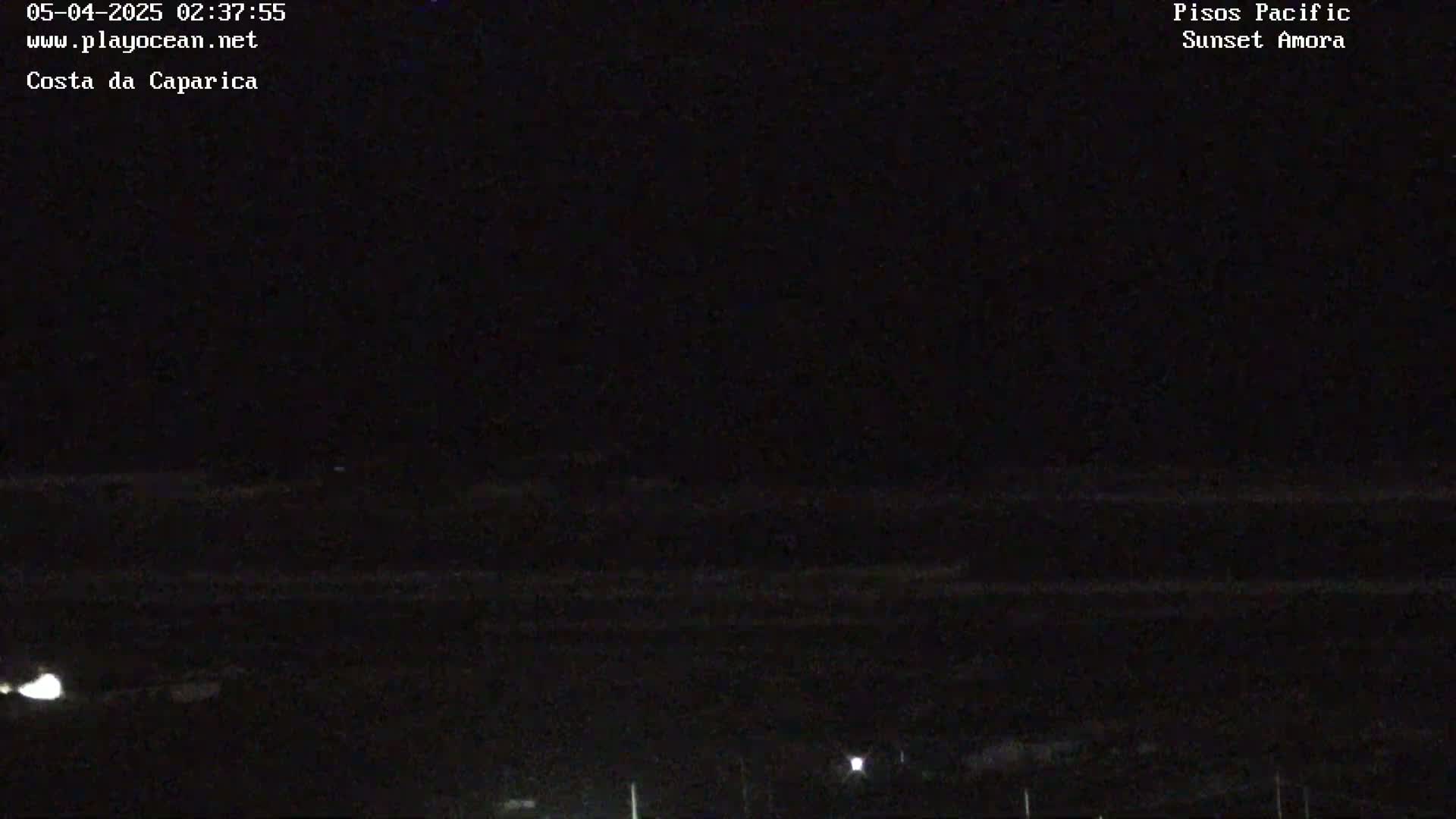 A dark, nighttime scene shows a mostly black expanse of ocean with faint lights visible in the distance.