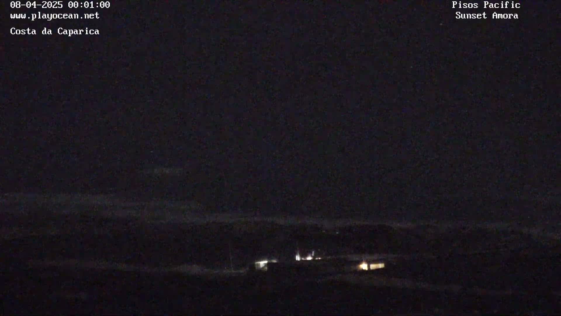A nighttime long shot shows a dark landscape with a few dimly lit structures and a dark sky.