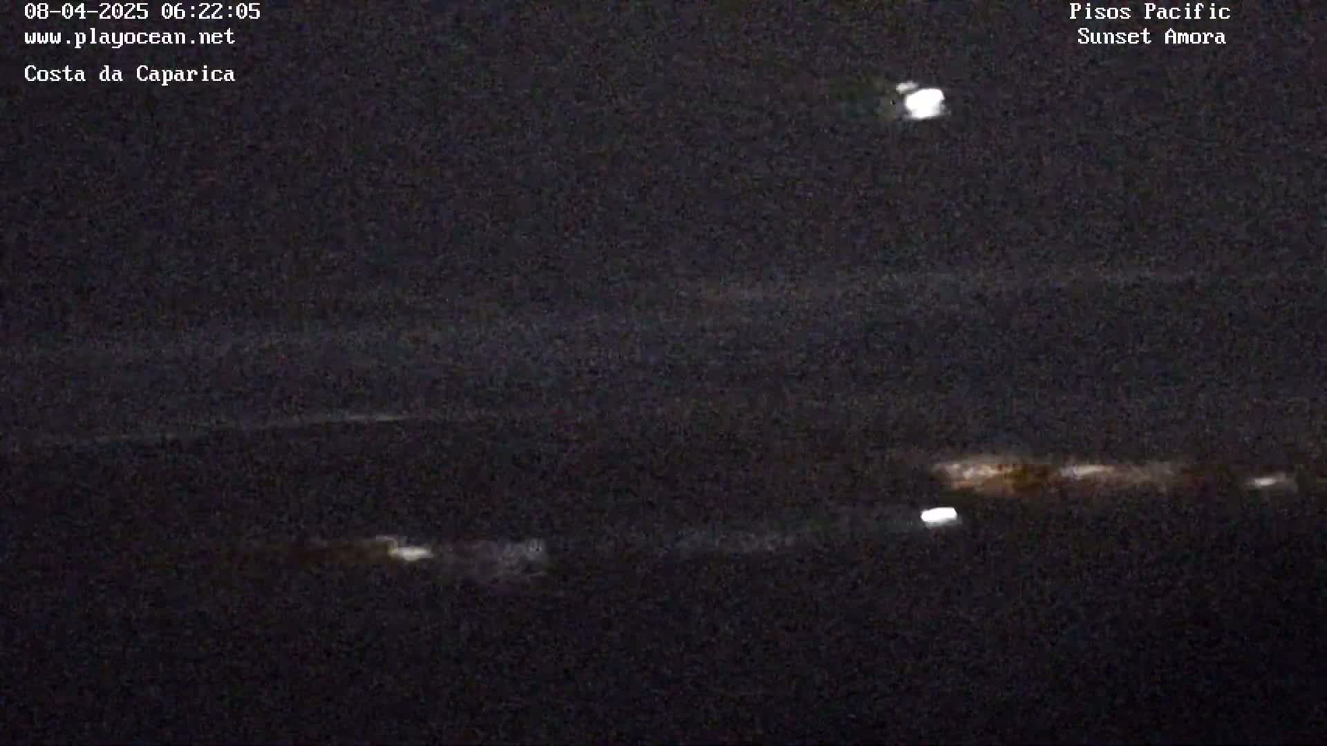 A nighttime, low-light view of a dark ocean with a few faint lights visible near the horizon.