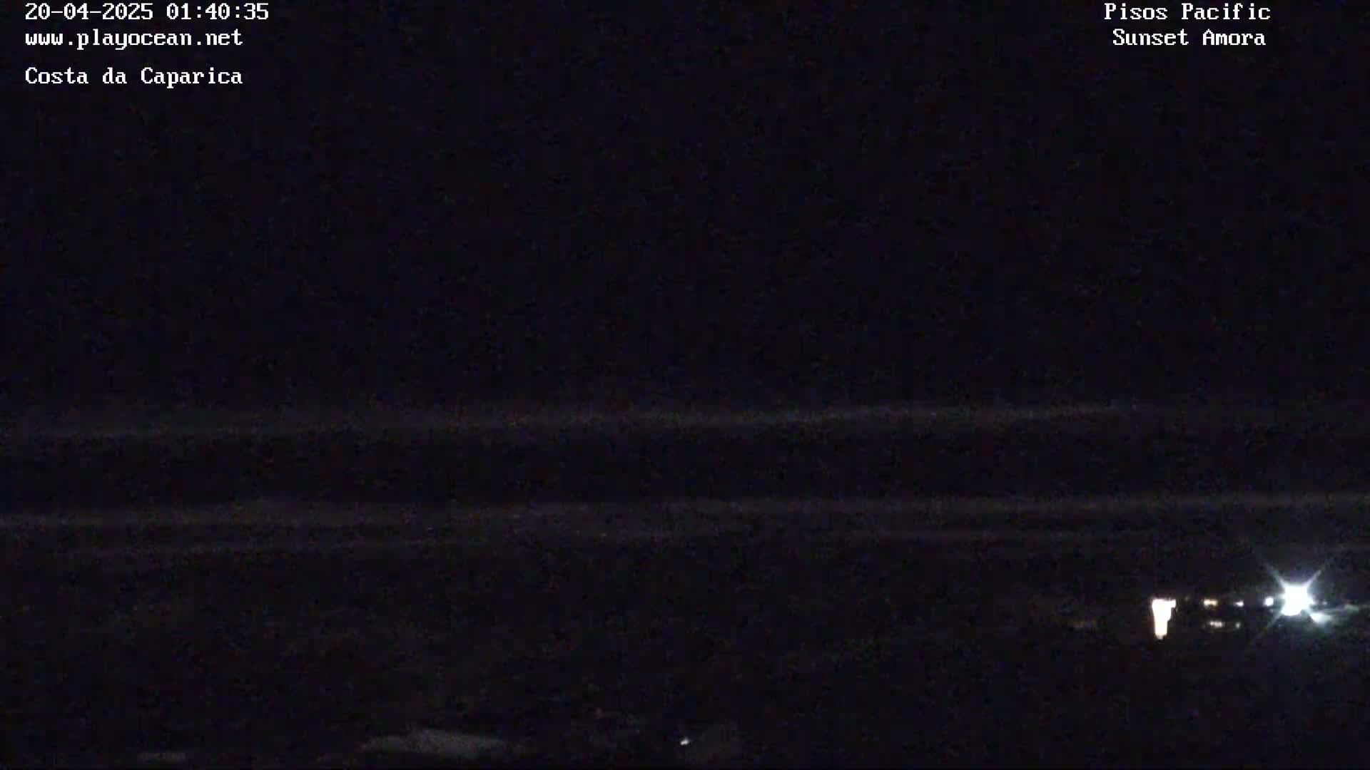 A dark nighttime coastal scene shows a mostly calm ocean with a few faint lights visible in the distance.