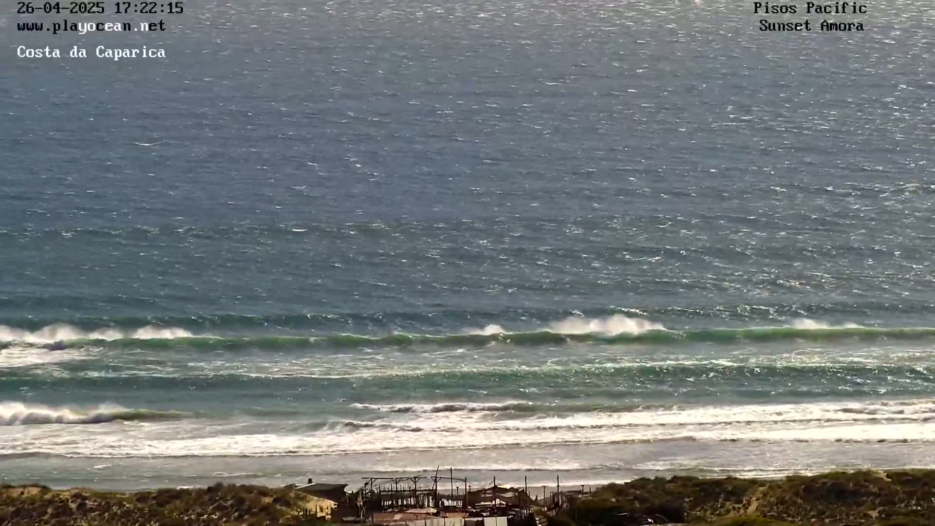 Ocean waves break on a sandy shore under a mostly clear sky.