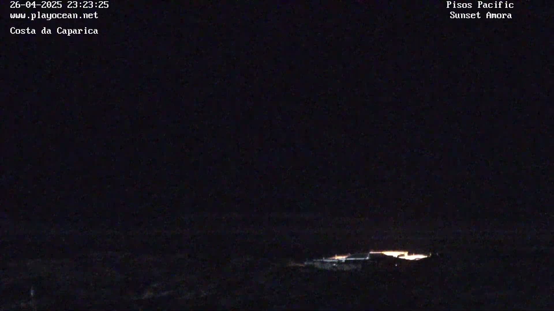 A nighttime, long shot of dimly lit buildings or structures along a dark coastline under a clear, dark sky.