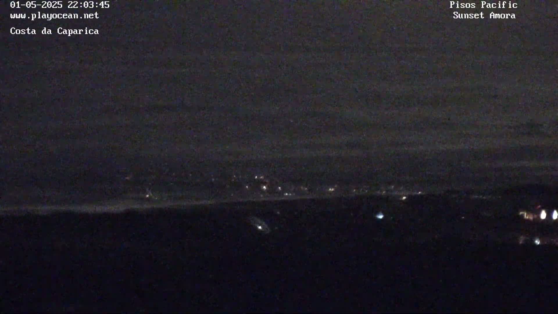 A nighttime long shot shows a distant city's lights faintly illuminating a dark, cloudy sky over a coastal area.