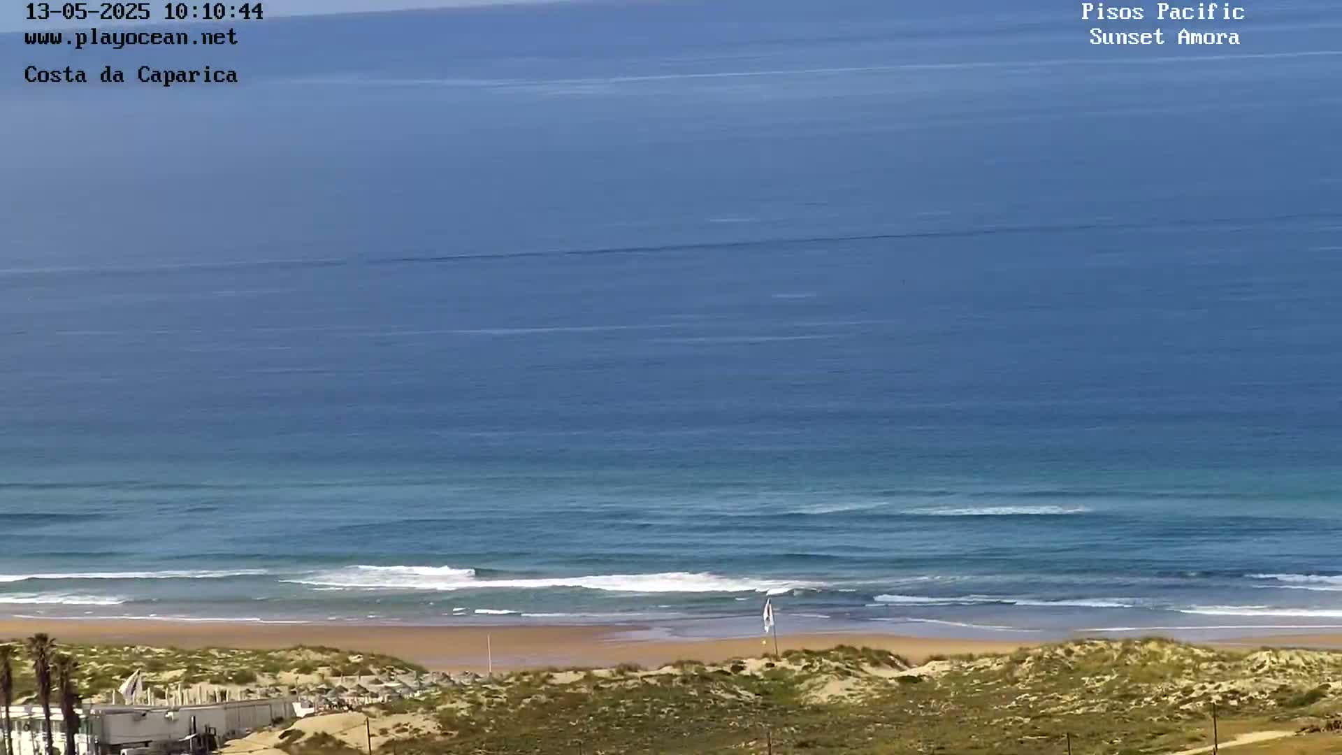 A sandy beach with small waves laps the shore of a calm, blue ocean under a clear sky.