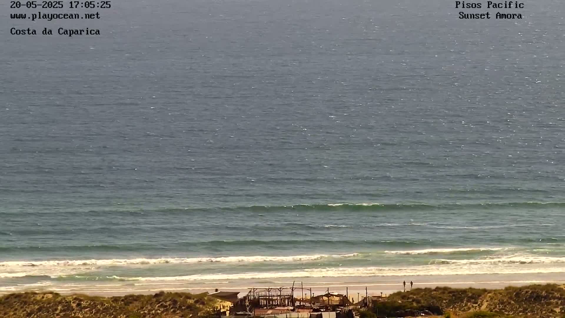 A long shot of an ocean beach with small waves gently rolling onto the shore on a sunny day.