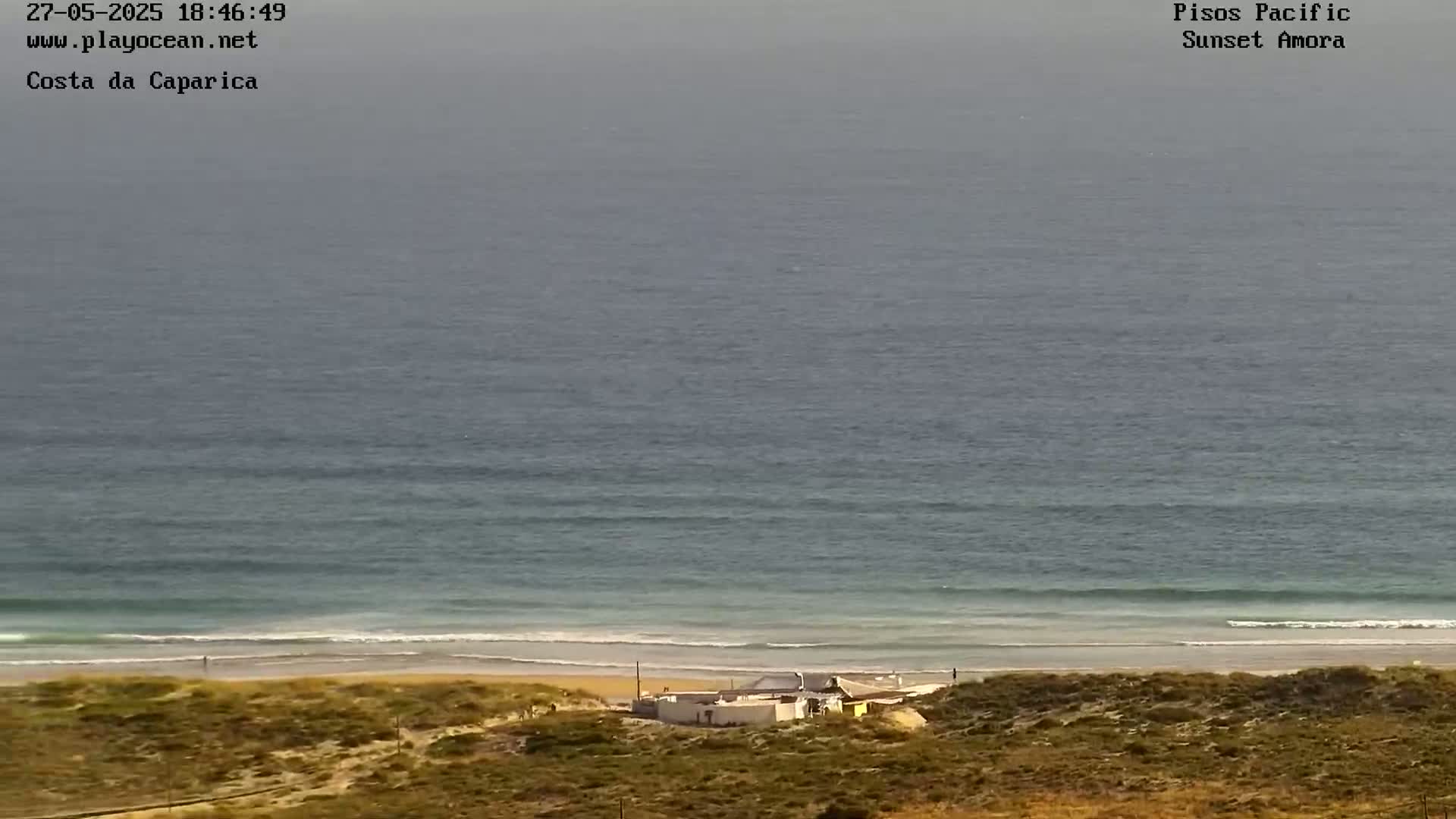 A beach with a building and rolling waves under an overcast sky.