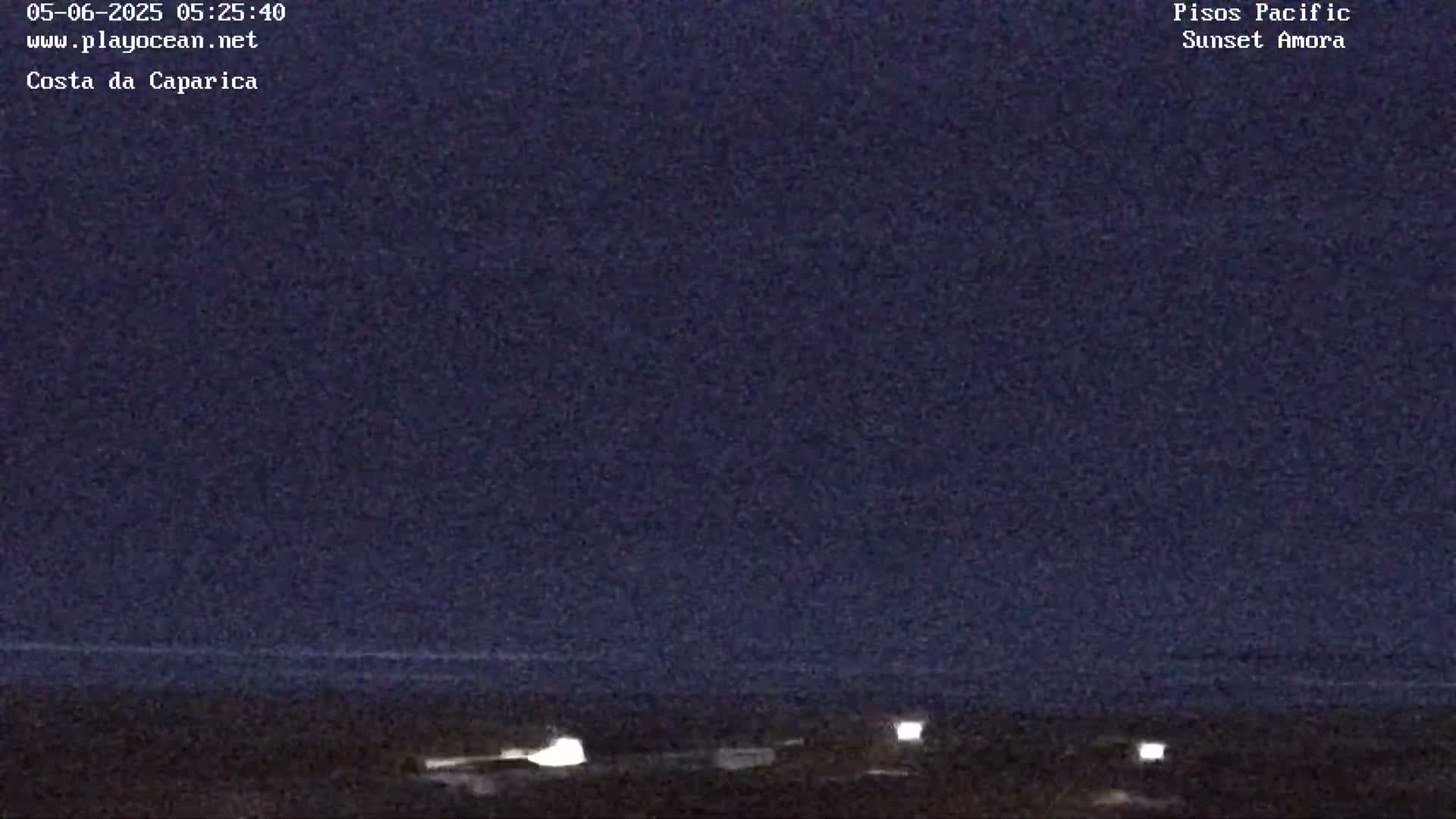 A dark, nighttime scene shows a flat expanse of land and water under a mostly clear, dark blue sky.