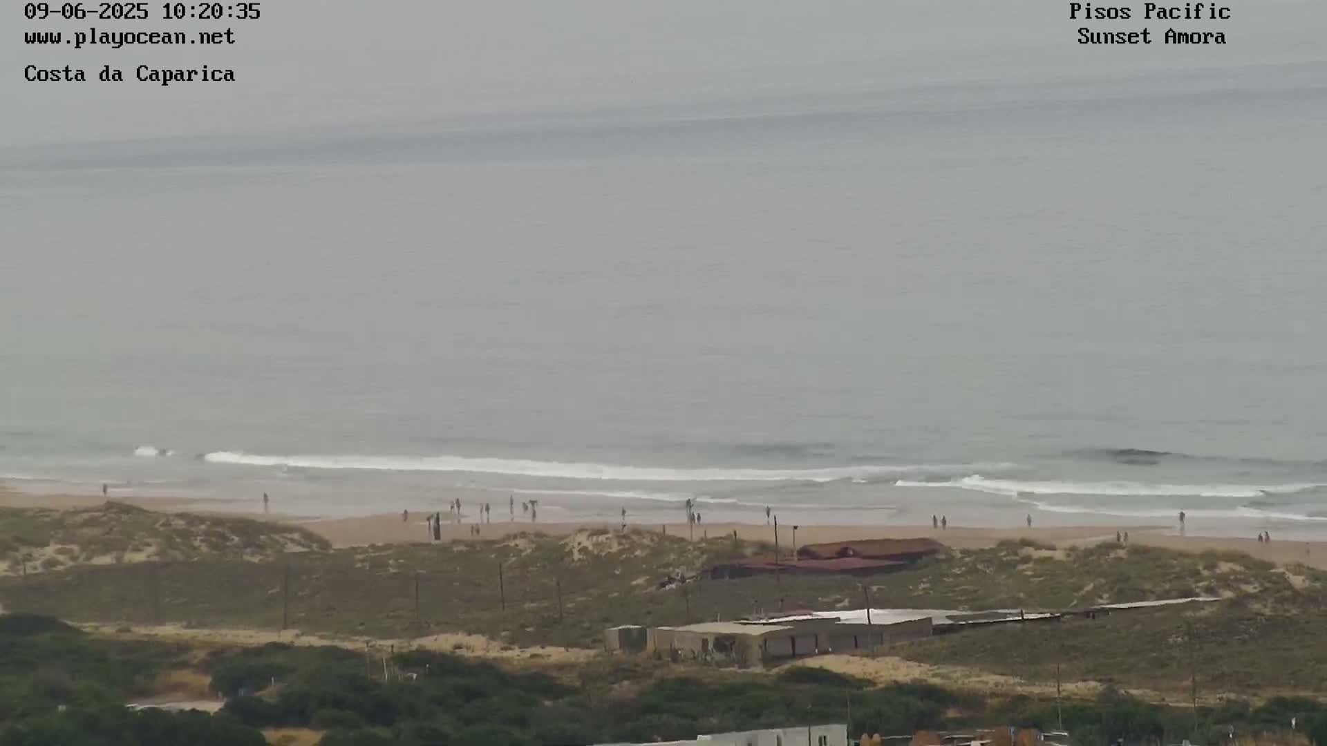 A beach with scattered people is visible under an overcast sky, with gentle waves rolling into the shore.