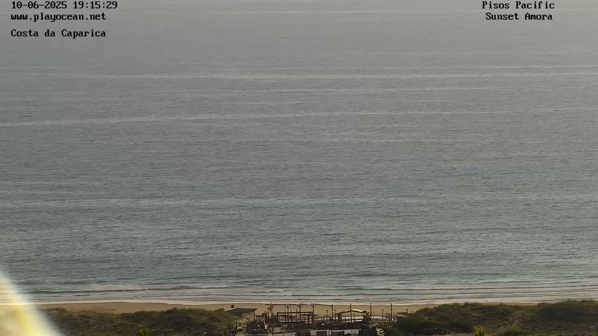 A beach with calm, gray water and a structure near the shoreline is visible from an elevated viewpoint.