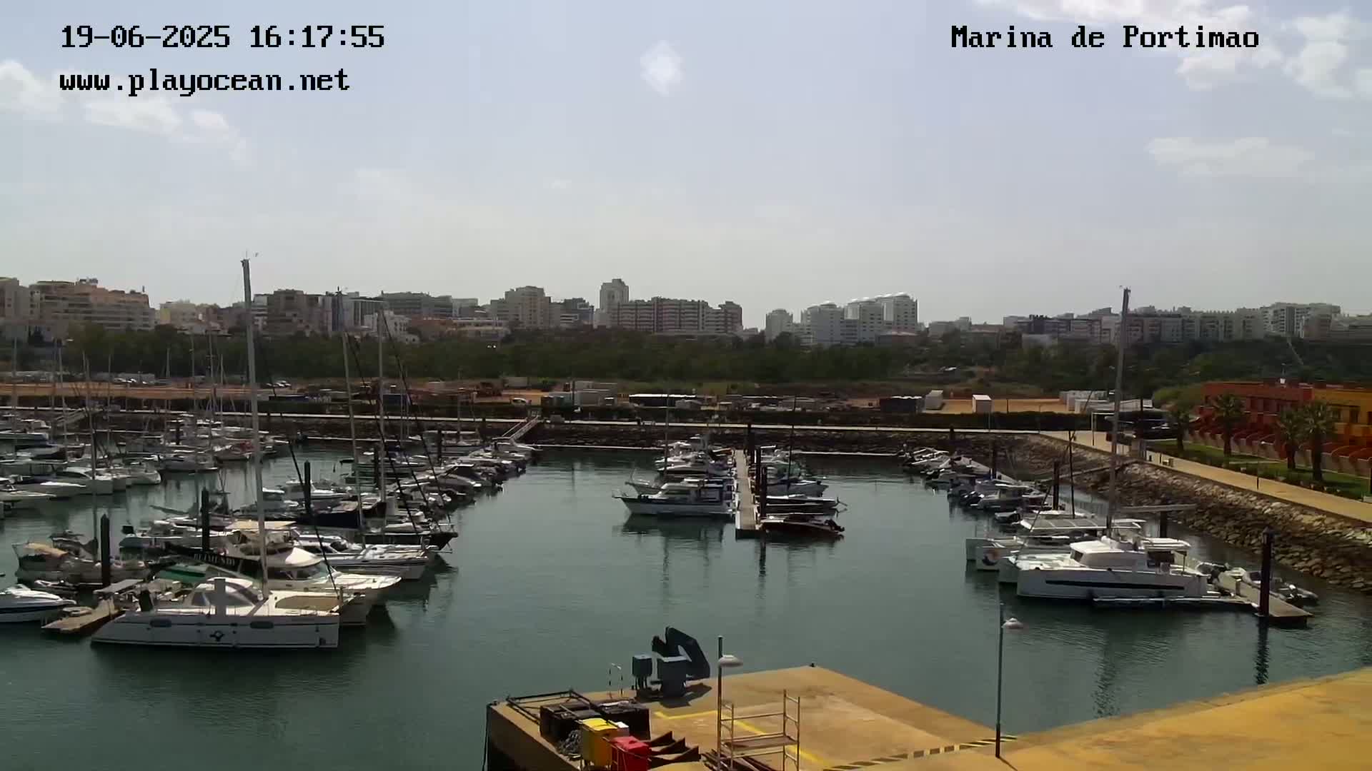A marina filled with numerous boats is situated in front of a city skyline under a partly cloudy sky.