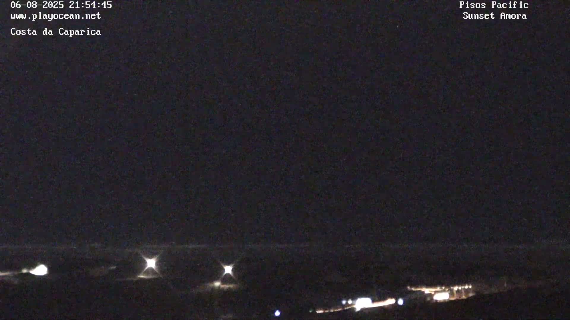 A nighttime long shot shows a dark landscape with a few bright lights in the distance along a dark horizon line under a clear, dark sky.