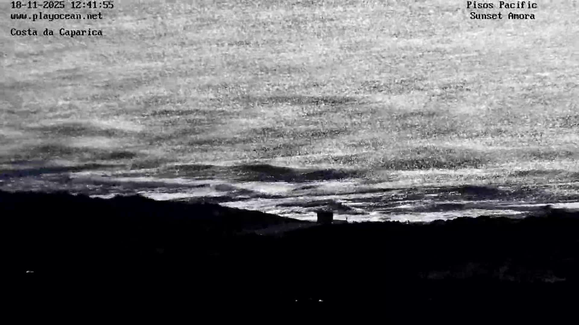 A nighttime long shot shows a dark landscape with a few bright lights in the distance along a dark horizon line under a clear, dark sky.