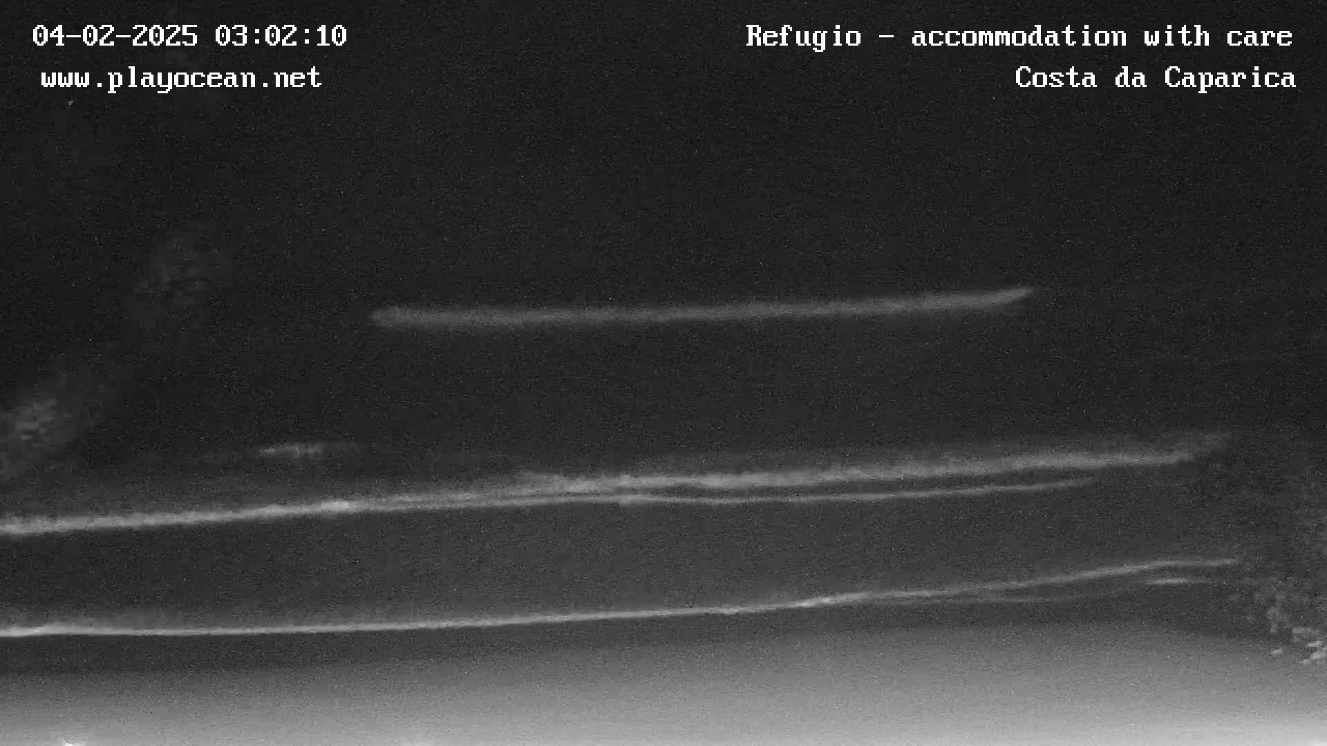 A nighttime, low-light image shows several faint horizontal lines of light on a dark body of water.
